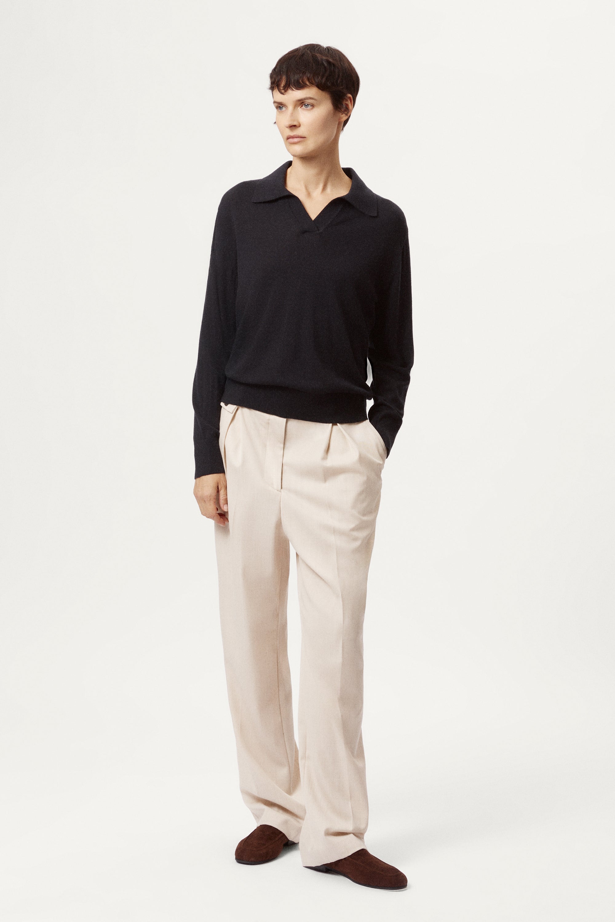 Person wearing a blue wool polo and beige pants on a white background