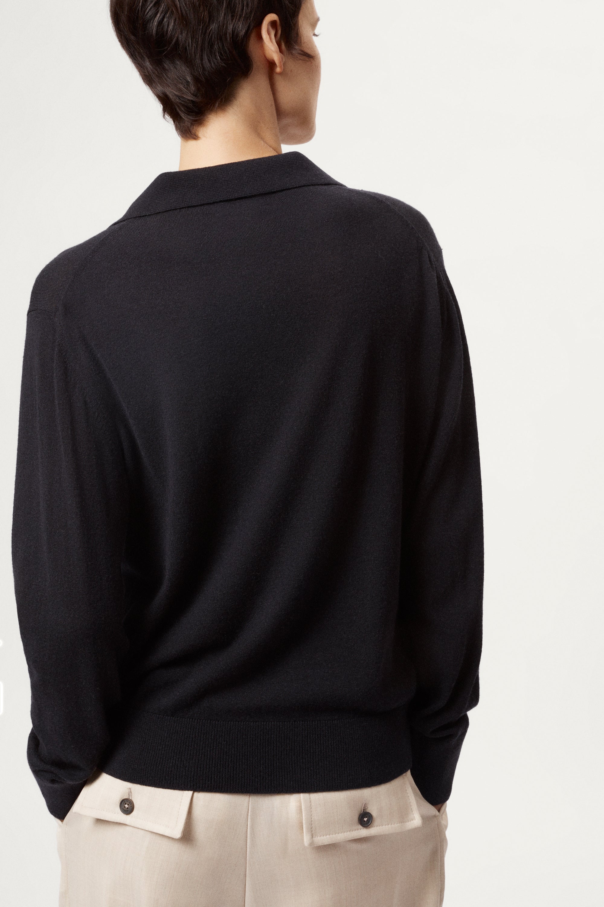 Person wearing a blue wool polo and beige pants on a white background