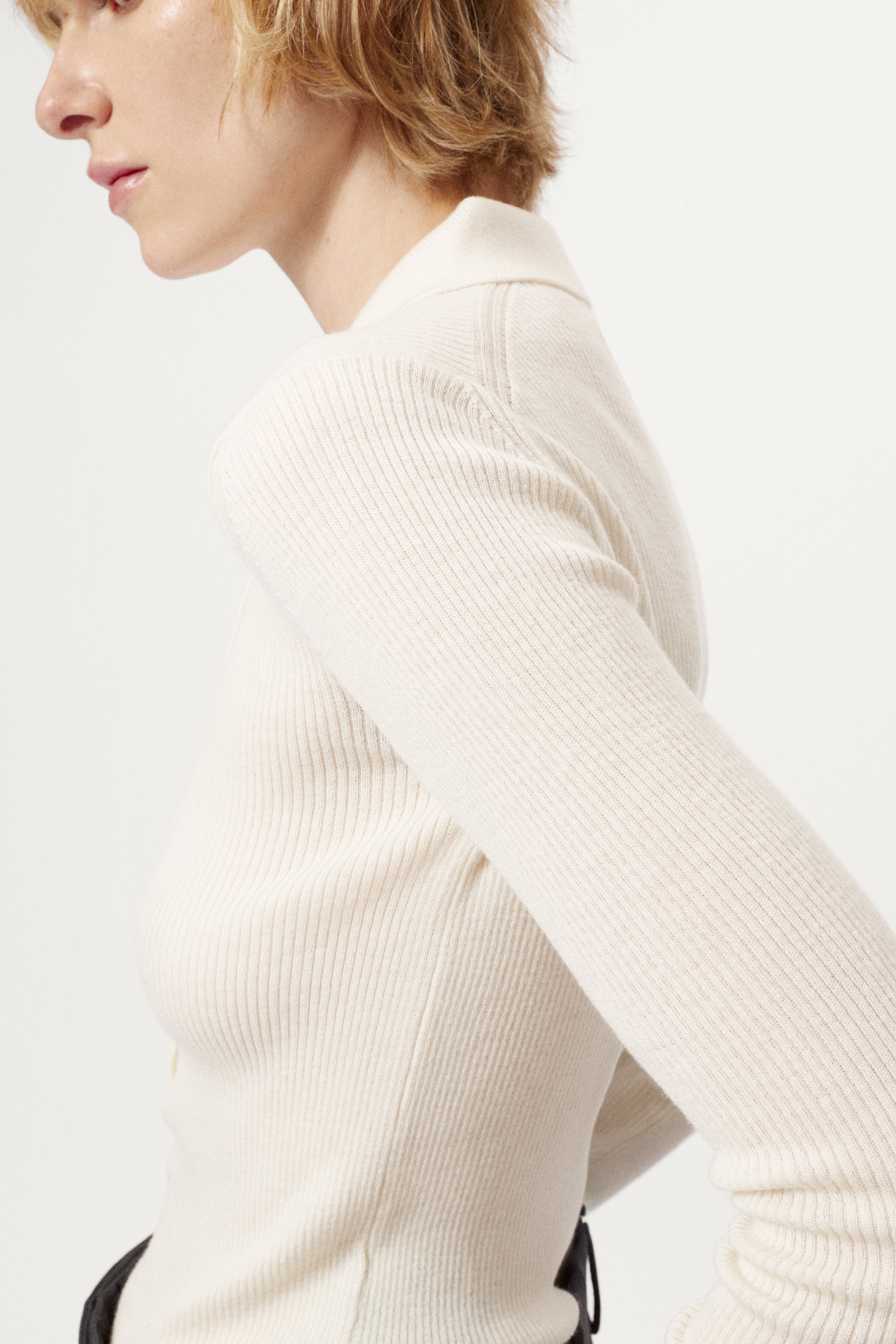 Woman wearing a white merino shirt and dark gray pants on a white background