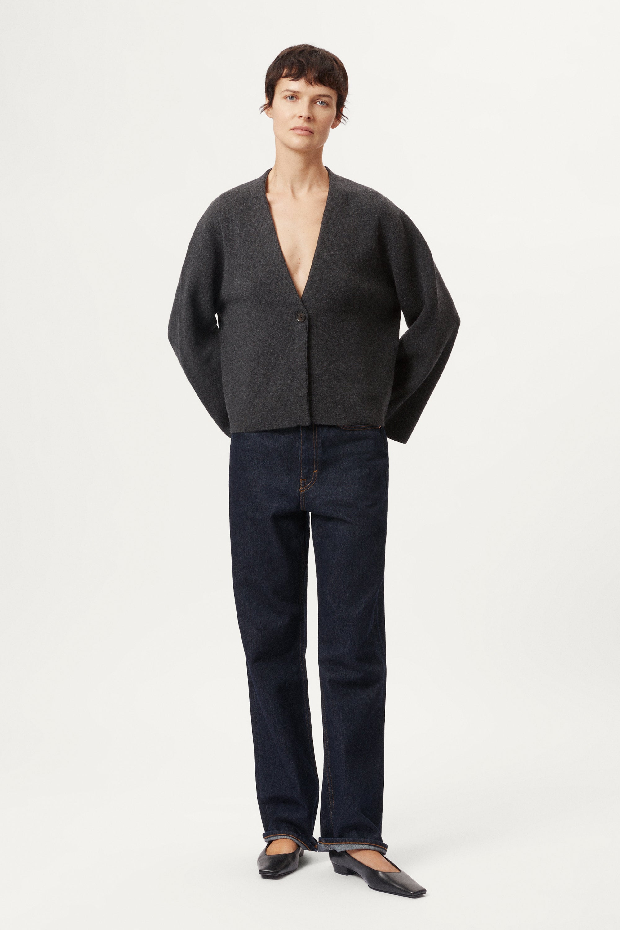 woman wearing a woolen dark gray cardigan with dark jeans on a white background