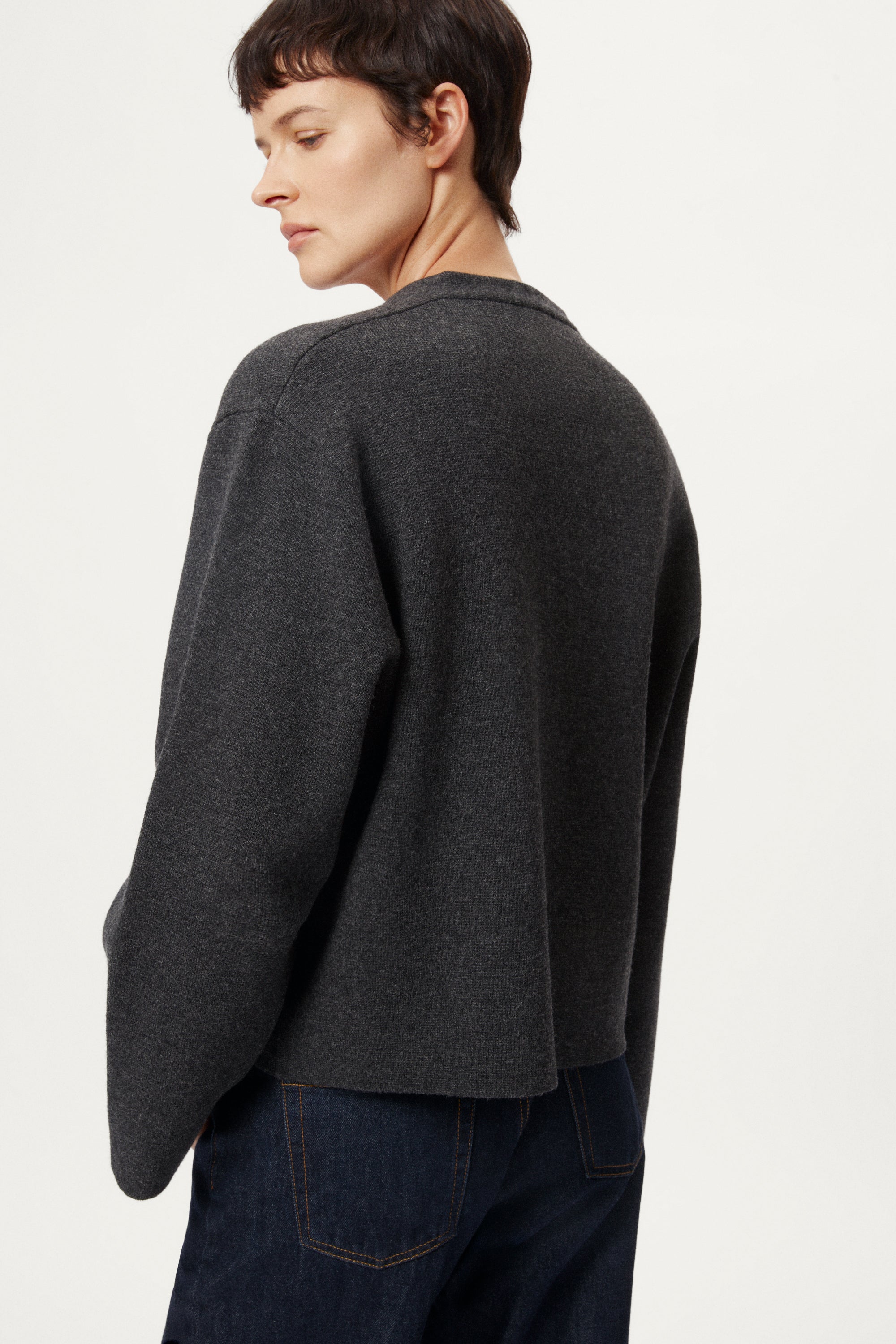 woman wearing a woolen dark gray cardigan with dark jeans on a white background
