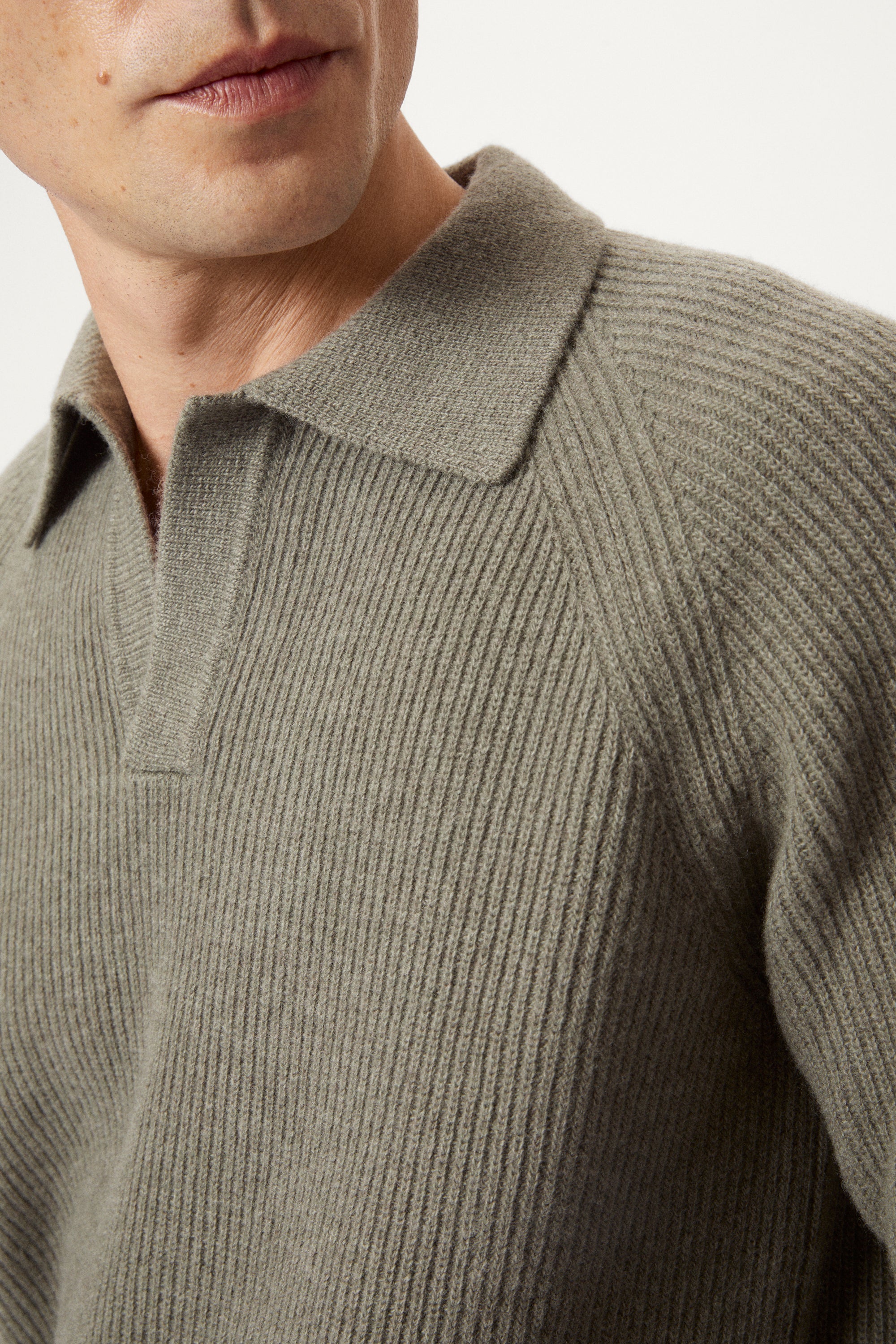 Close-up of a person wearing a green ribbed sweater with a collar.