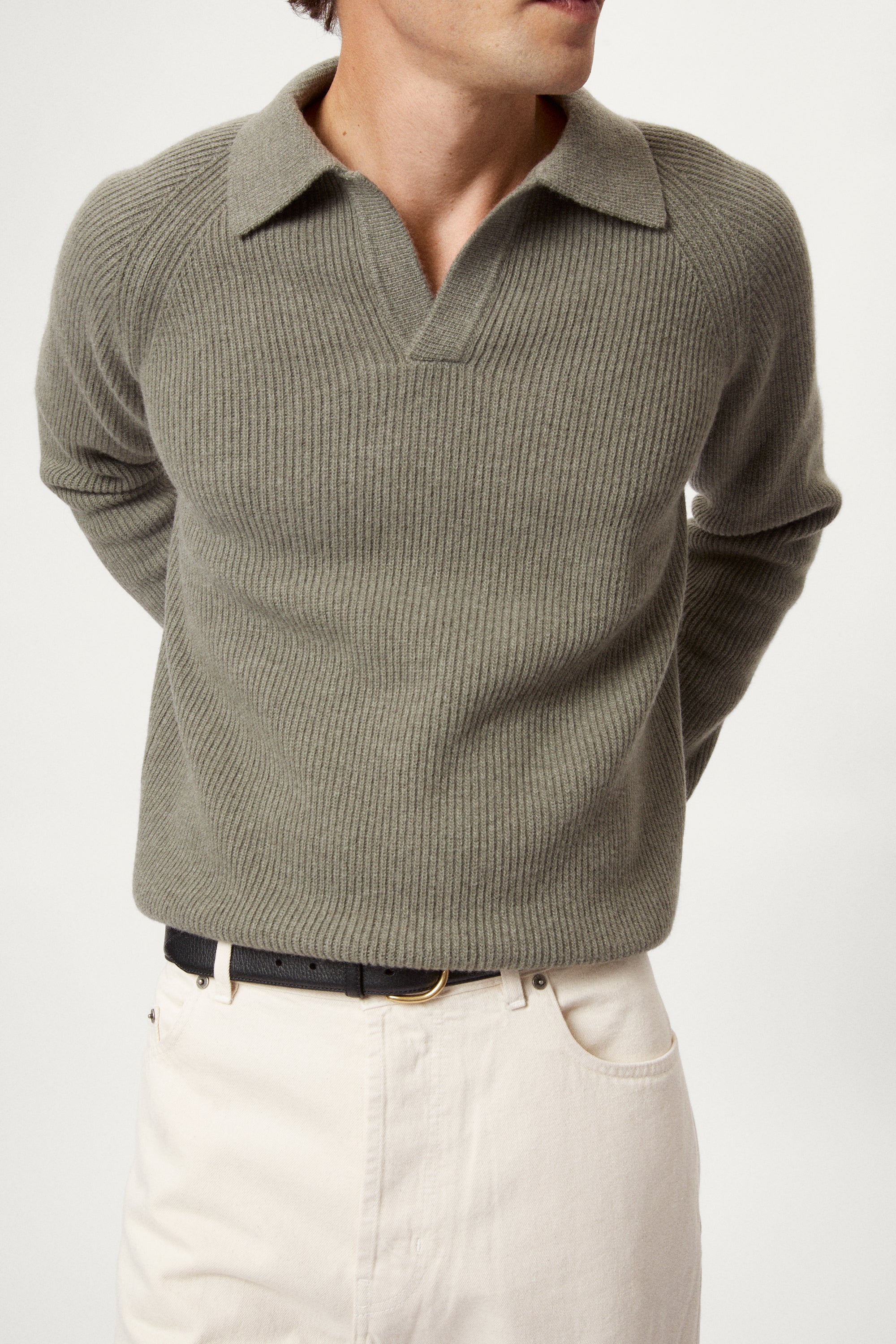 Man wearing a wool green polo sweater sweater and white pants on a white background
