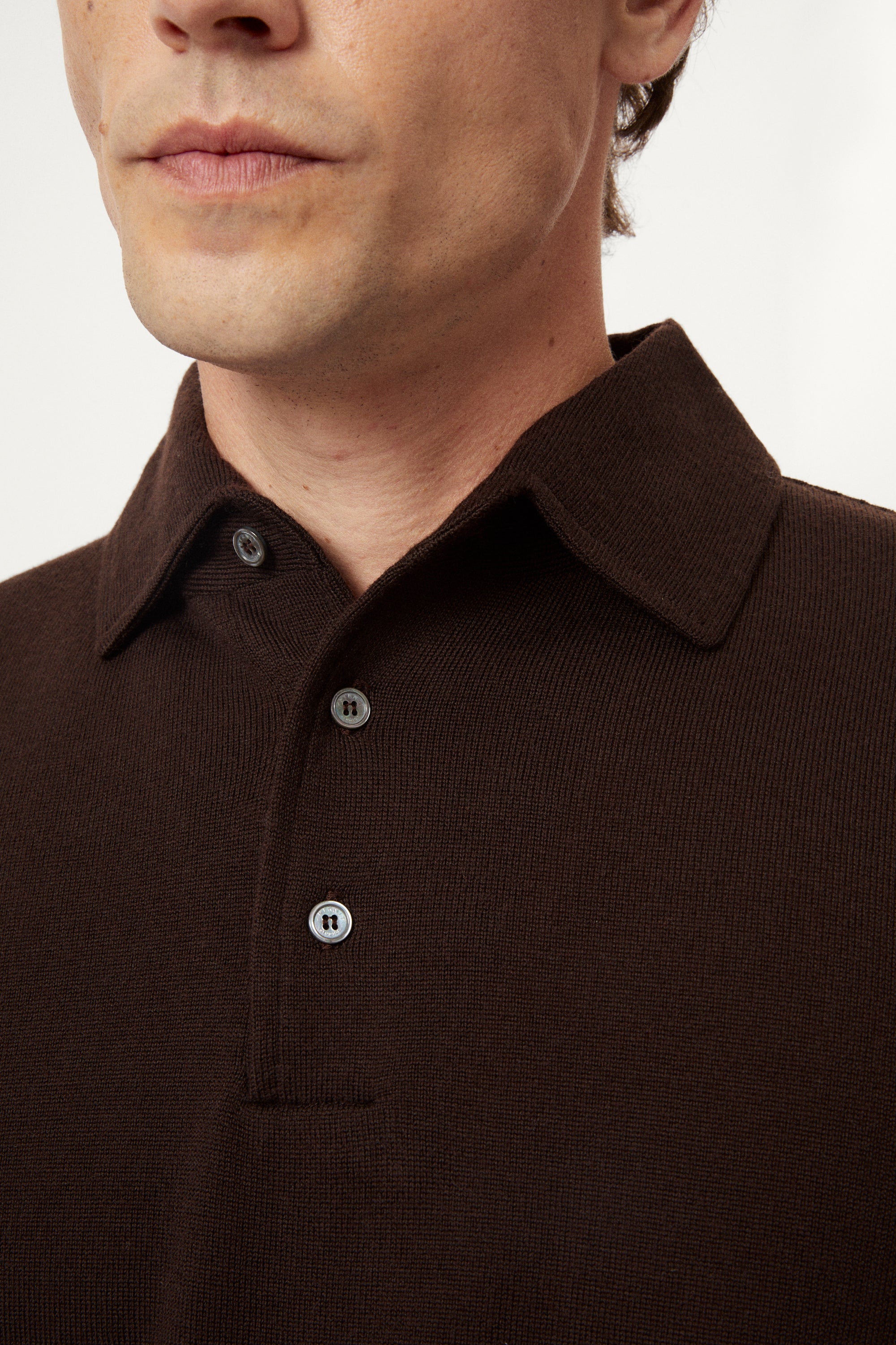 Close-up of a person wearing a brown polo with a plain background