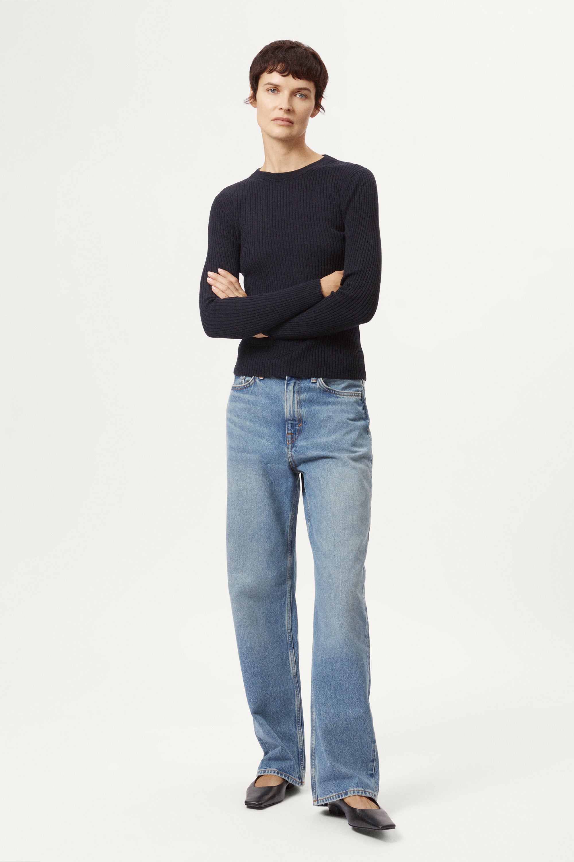 Woman wearing a blue sweater and light blue jeans on a white background