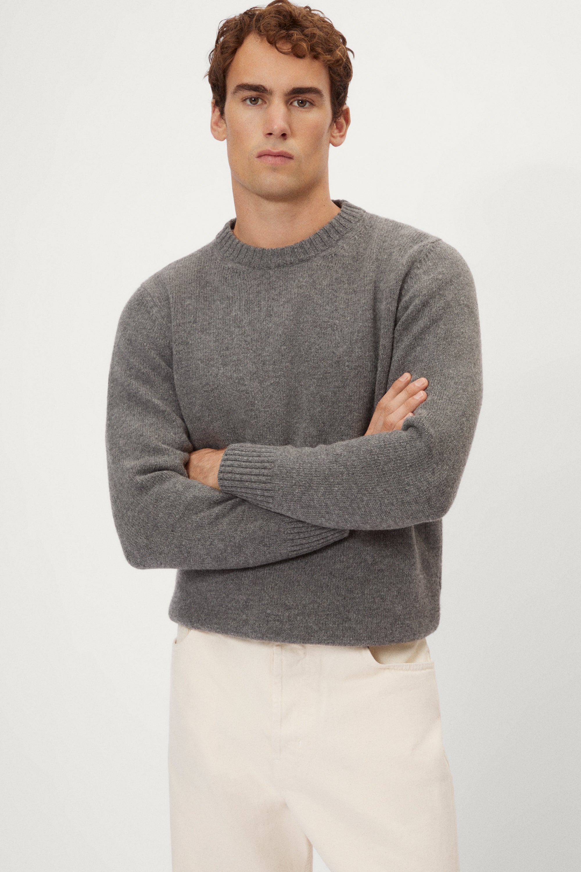 Man wearing a gray woolen sweater and white pants against a white background