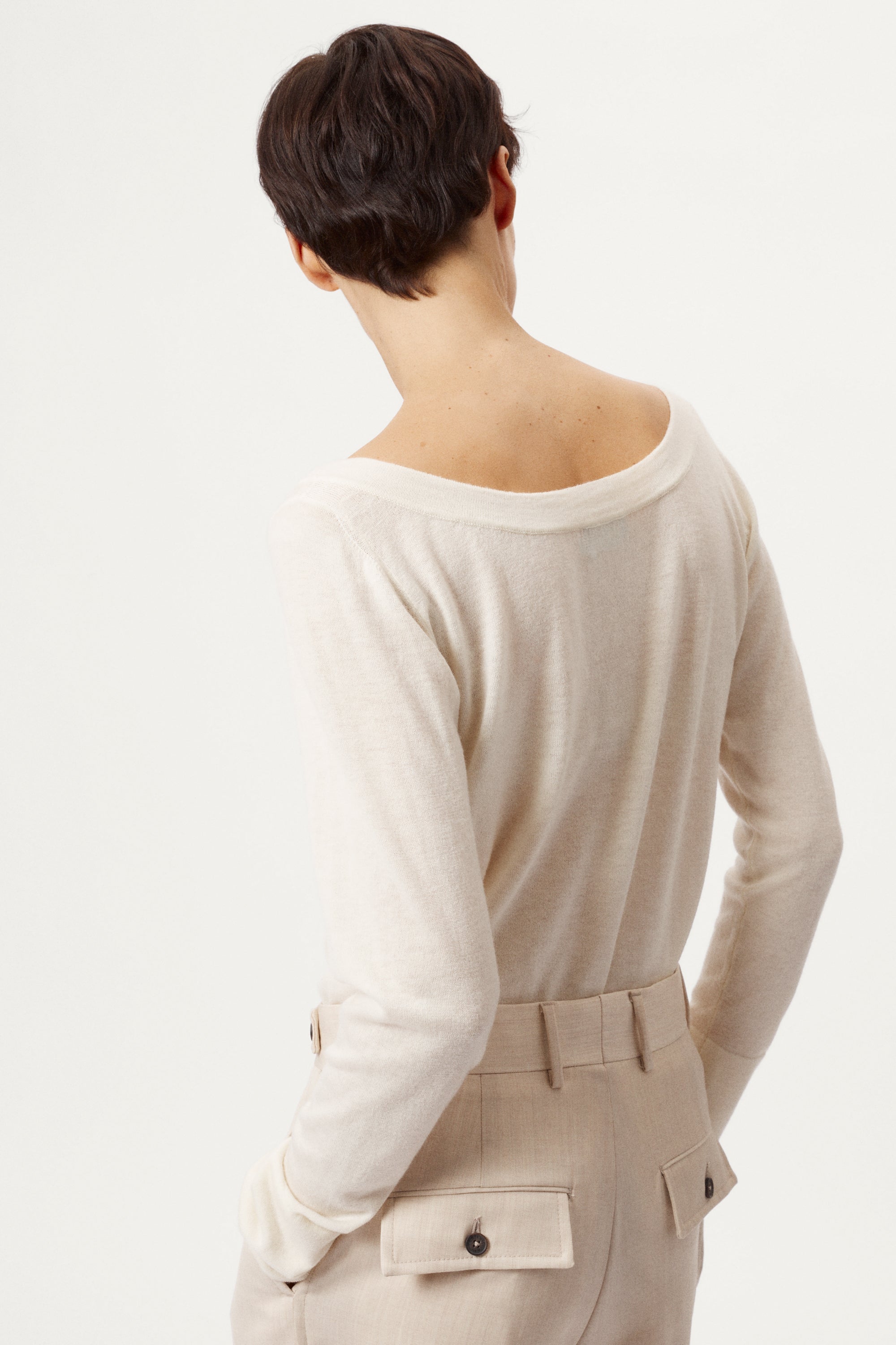 Person wearing a beige long-sleeve top with a plain background