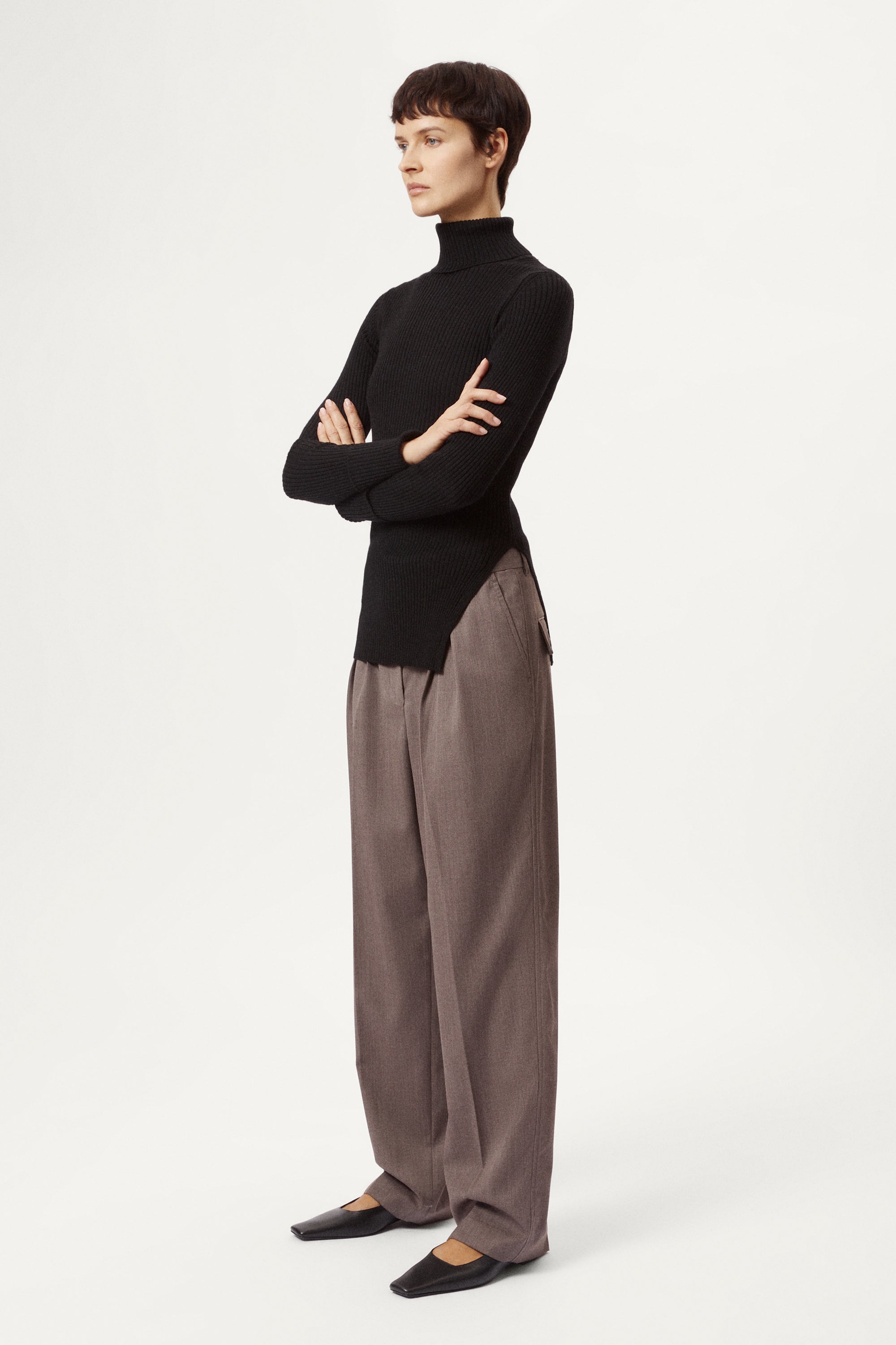 Person wearing a black turtleneck and brown pants on a white background