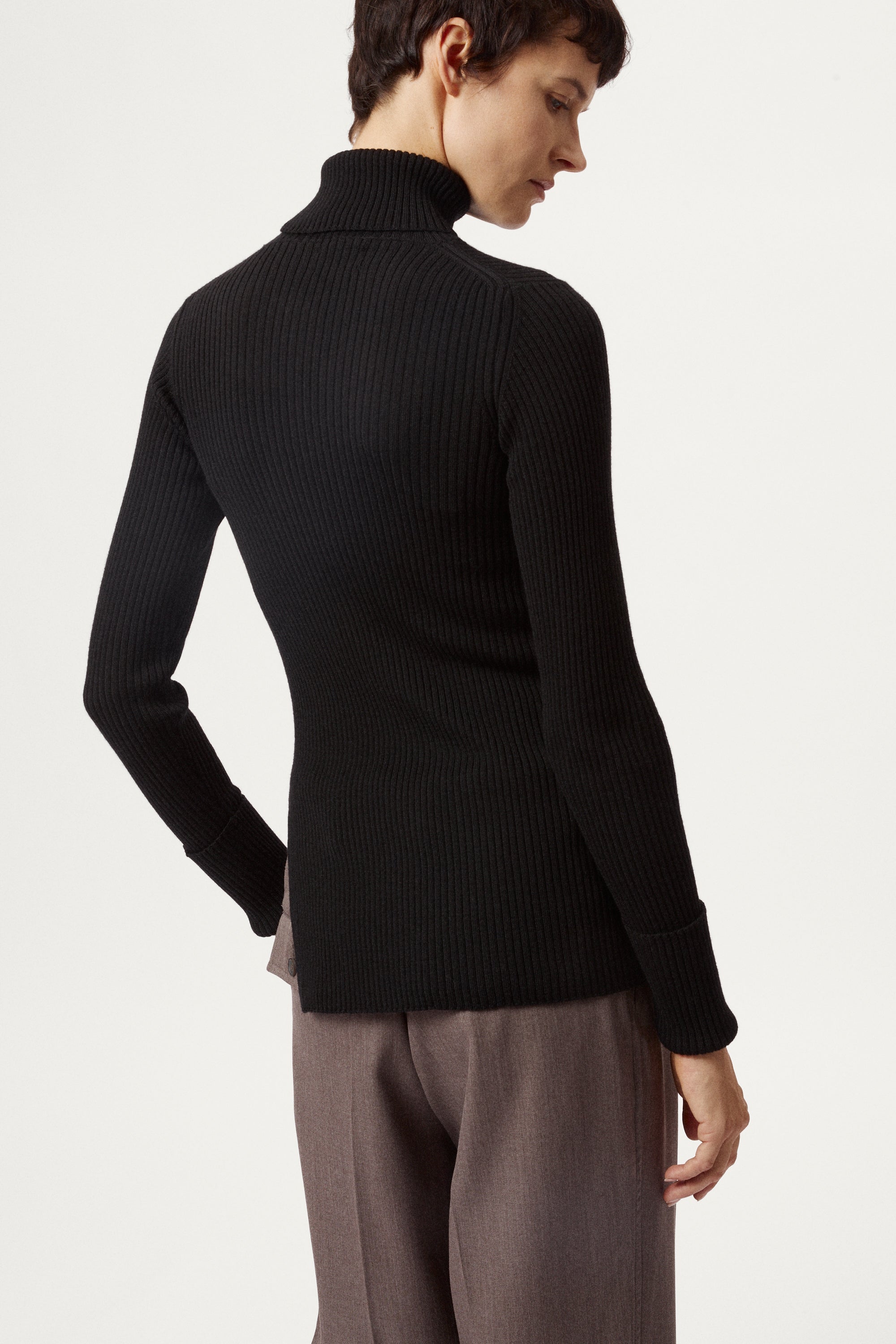 Person wearing a black turtleneck sweater and light brown pants on a white background