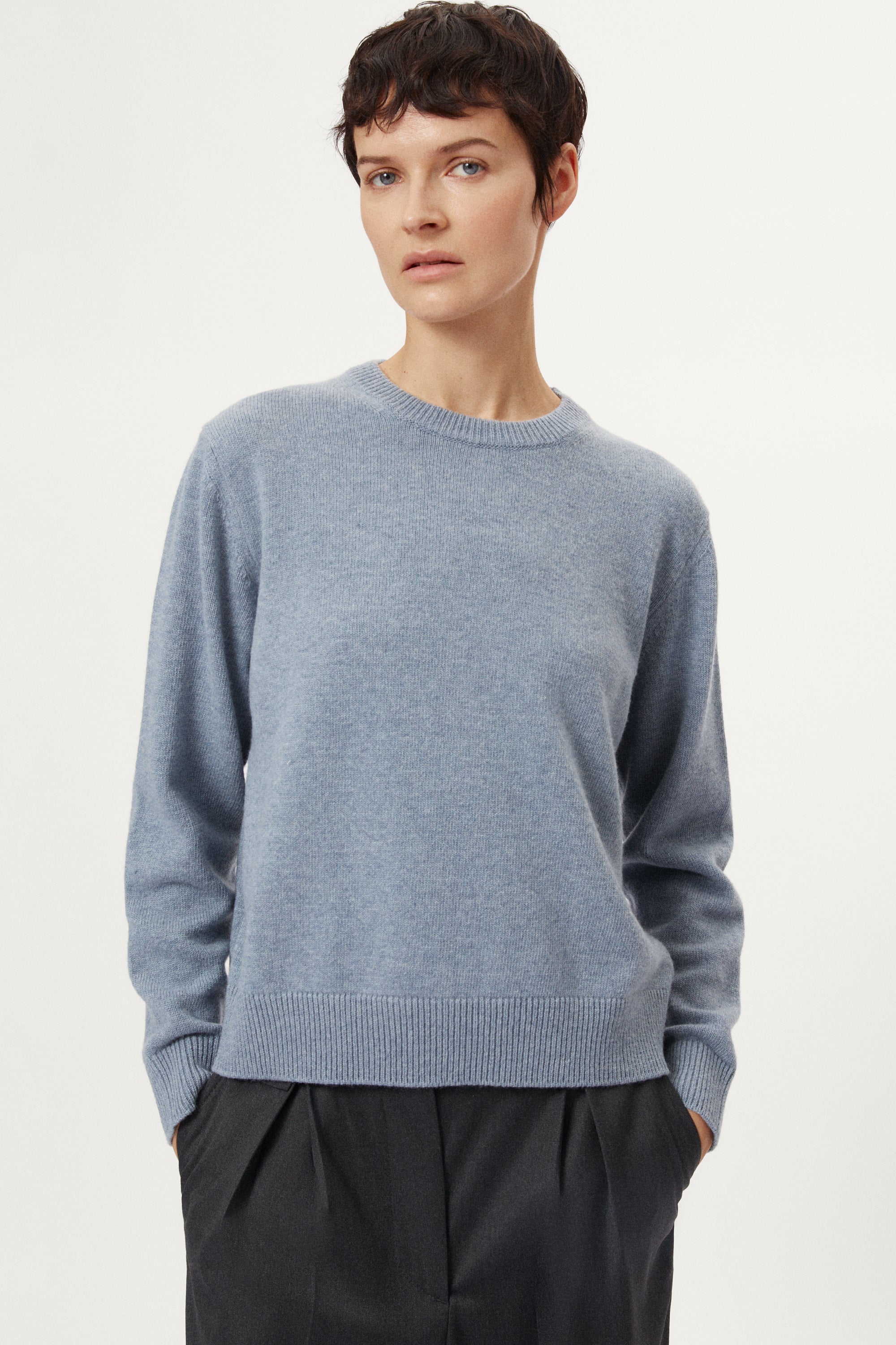 woman wearing a woolen light blue sweater and dark pants on a white background