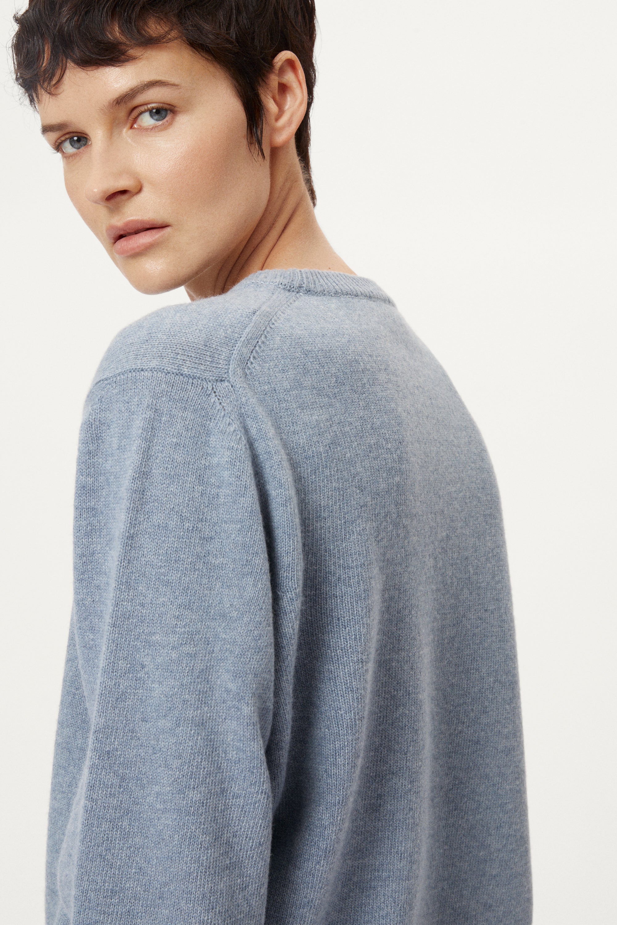 woman wearing a woolen light blue sweater and dark pants on a white background