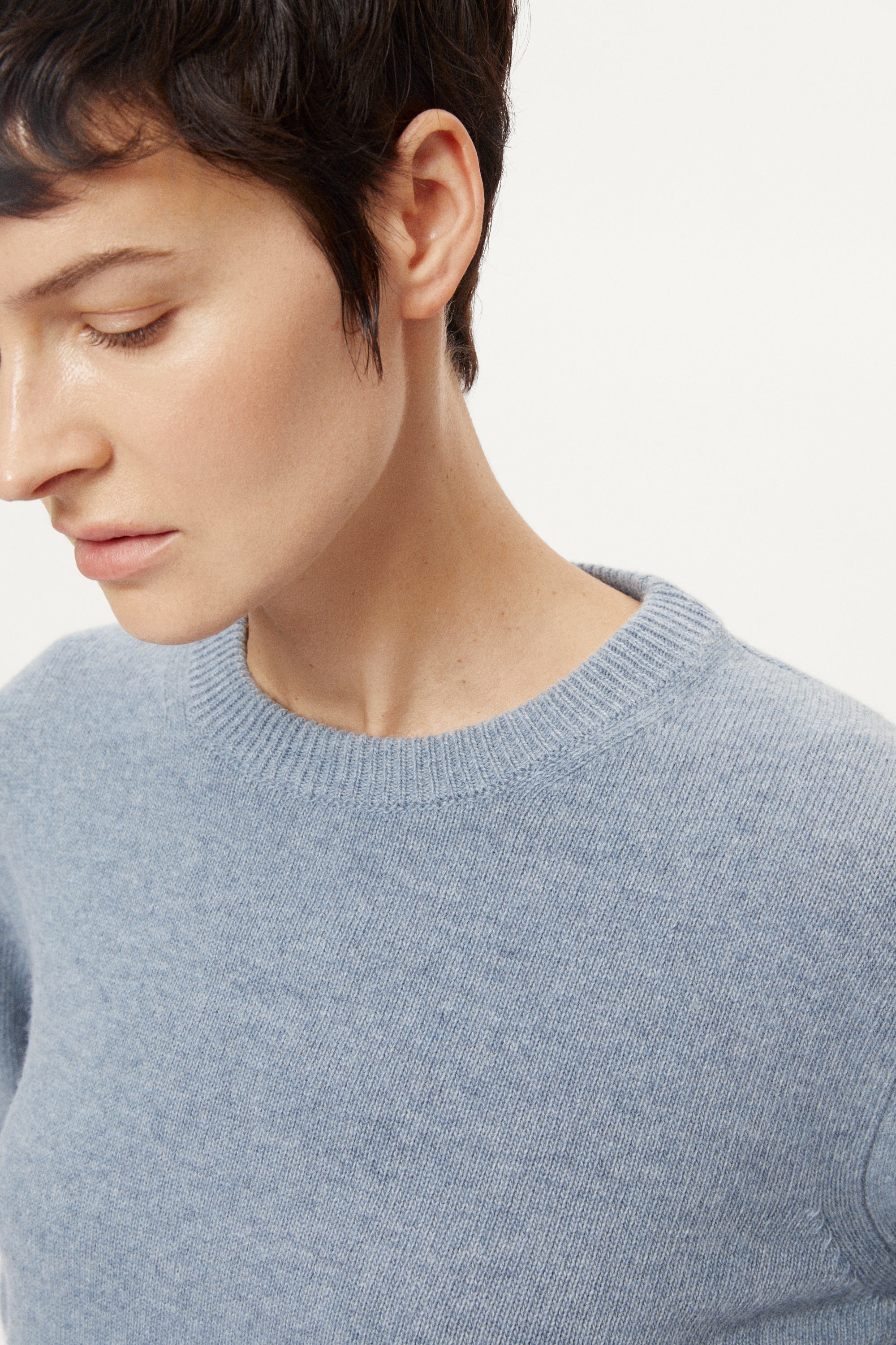 woman wearing a woolen light blue sweater and dark pants on a white background
