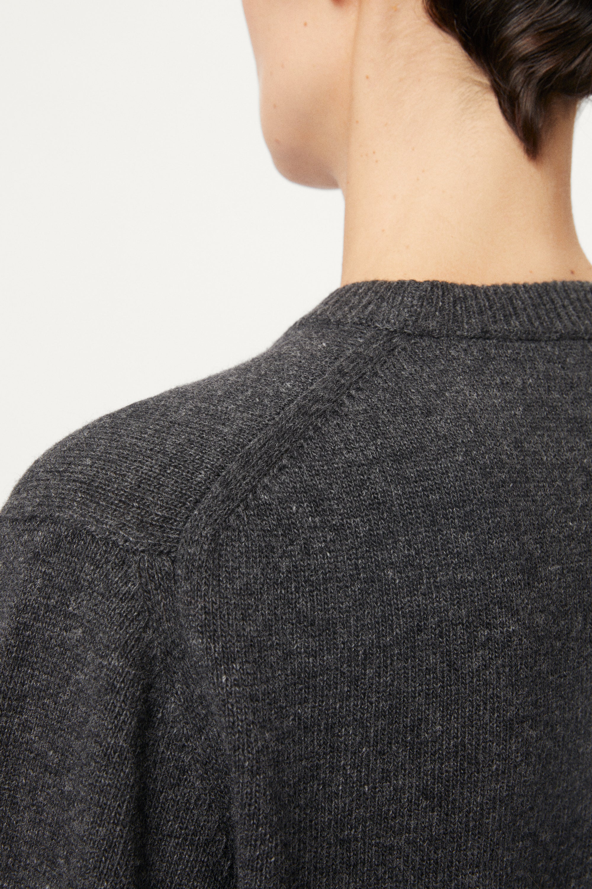 Close-up of a person wearing a dark gray sweater on a light gray background