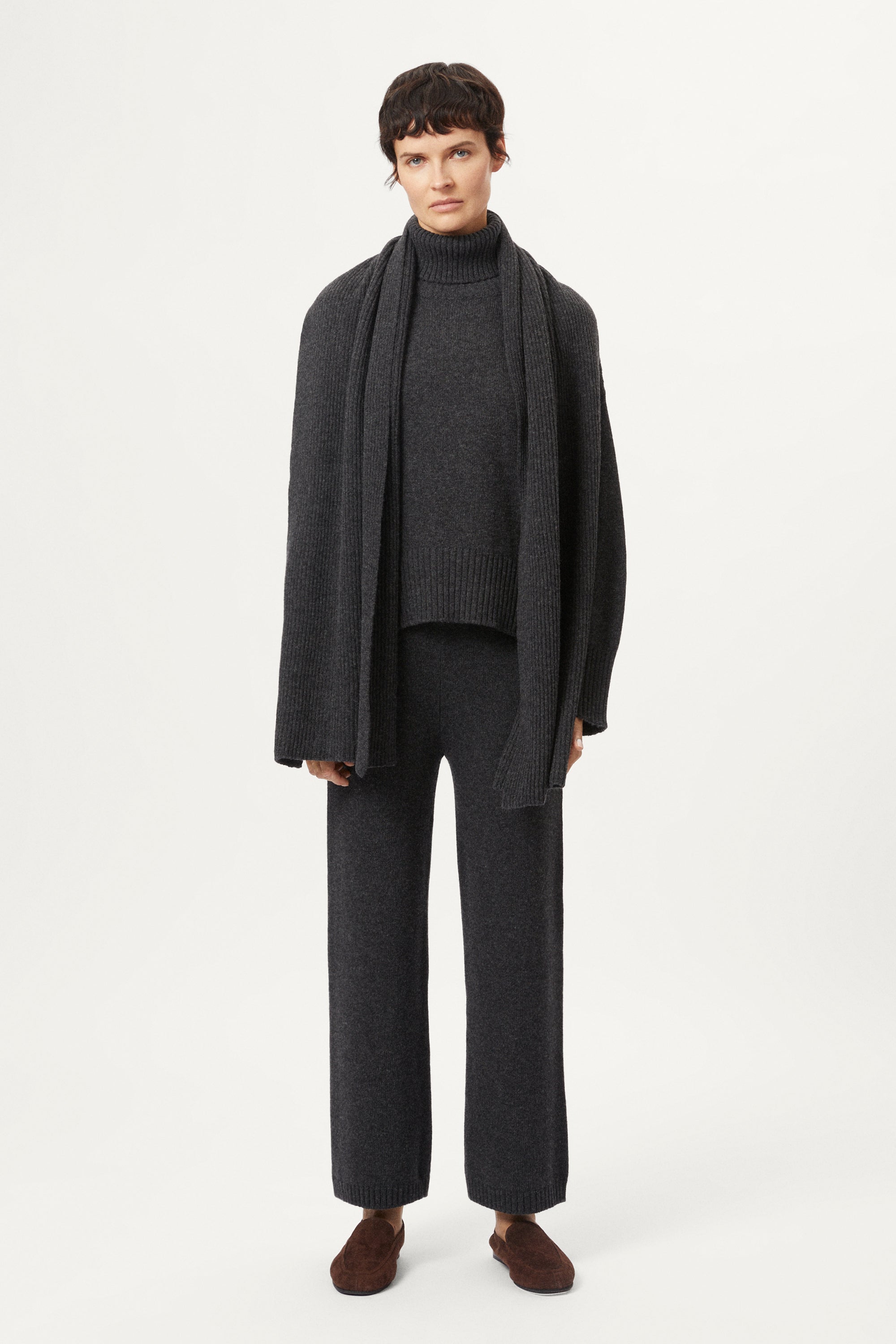 Woman wearing a woolen dark gray sweater and pants with brown shoes on a white background