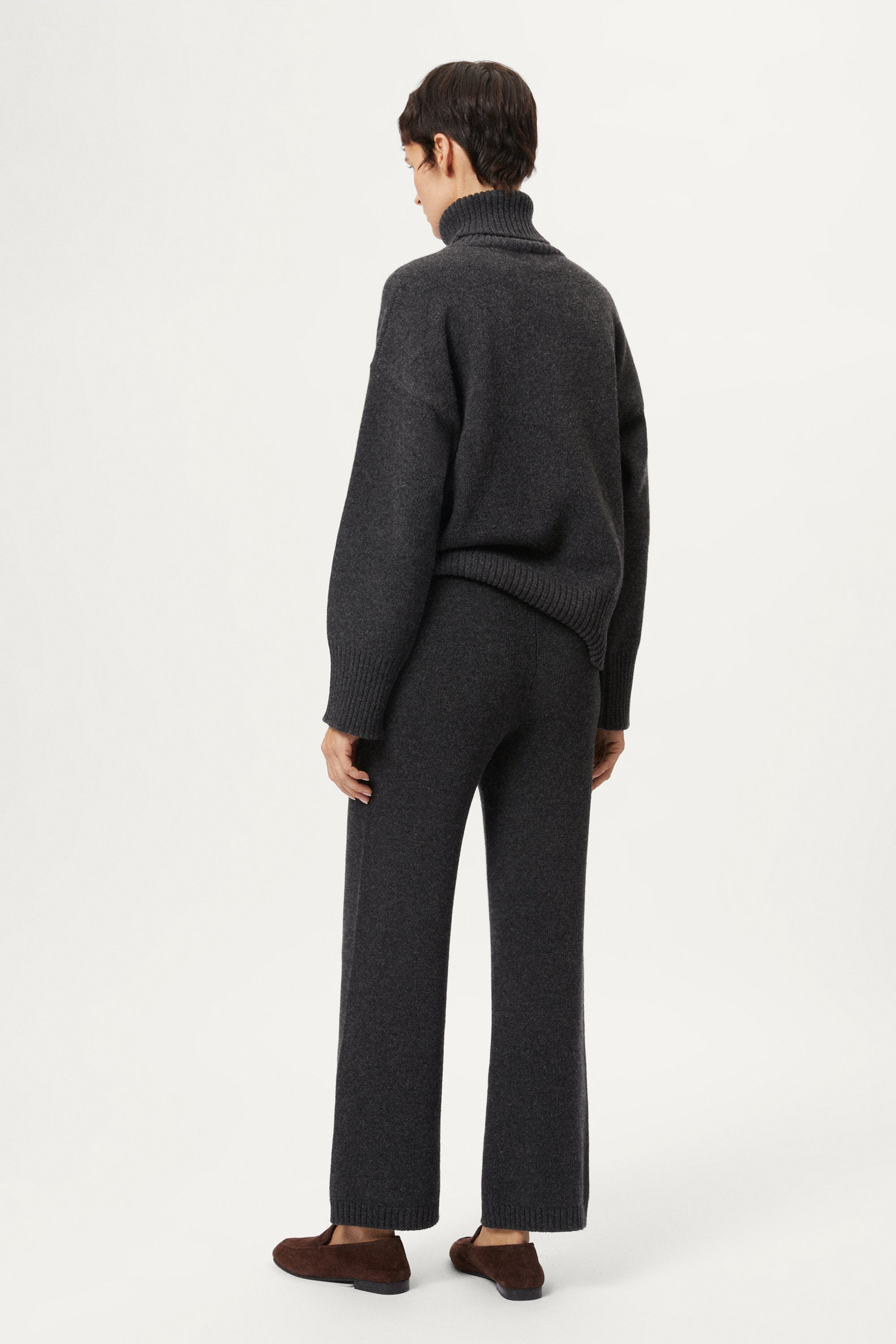 Woman wearing a woolen dark gray sweater and pants with brown shoes on a white background