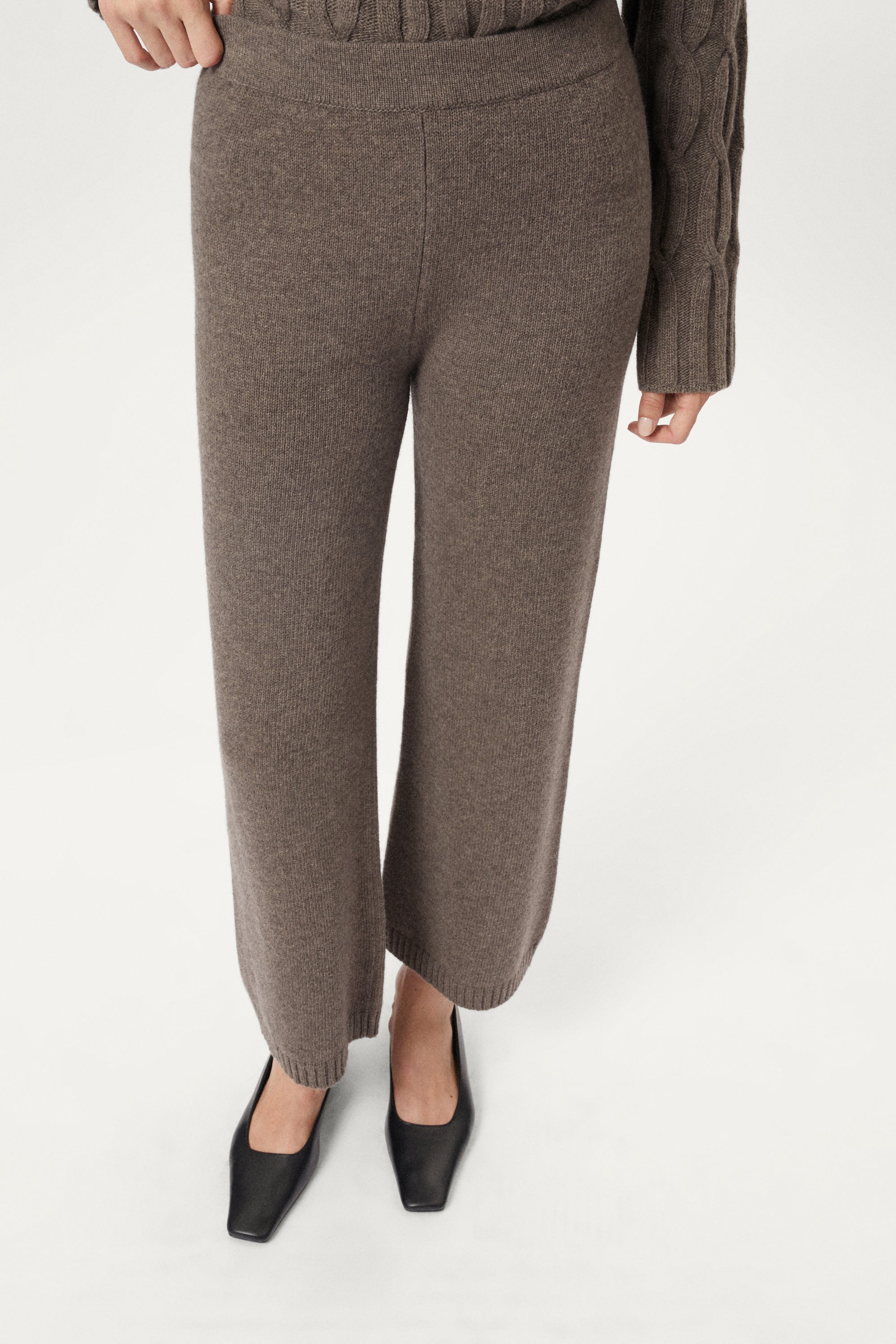 Brown woolen knitted pants worn by a person on a white background