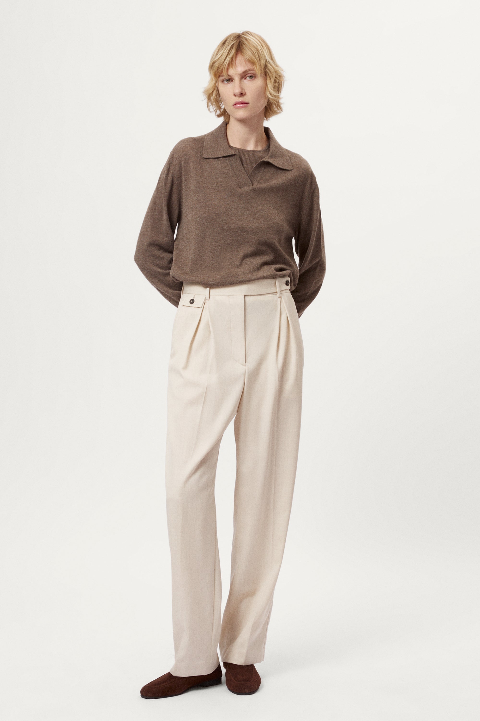 Woman wearing a brown sweater and beige pants on a white background
