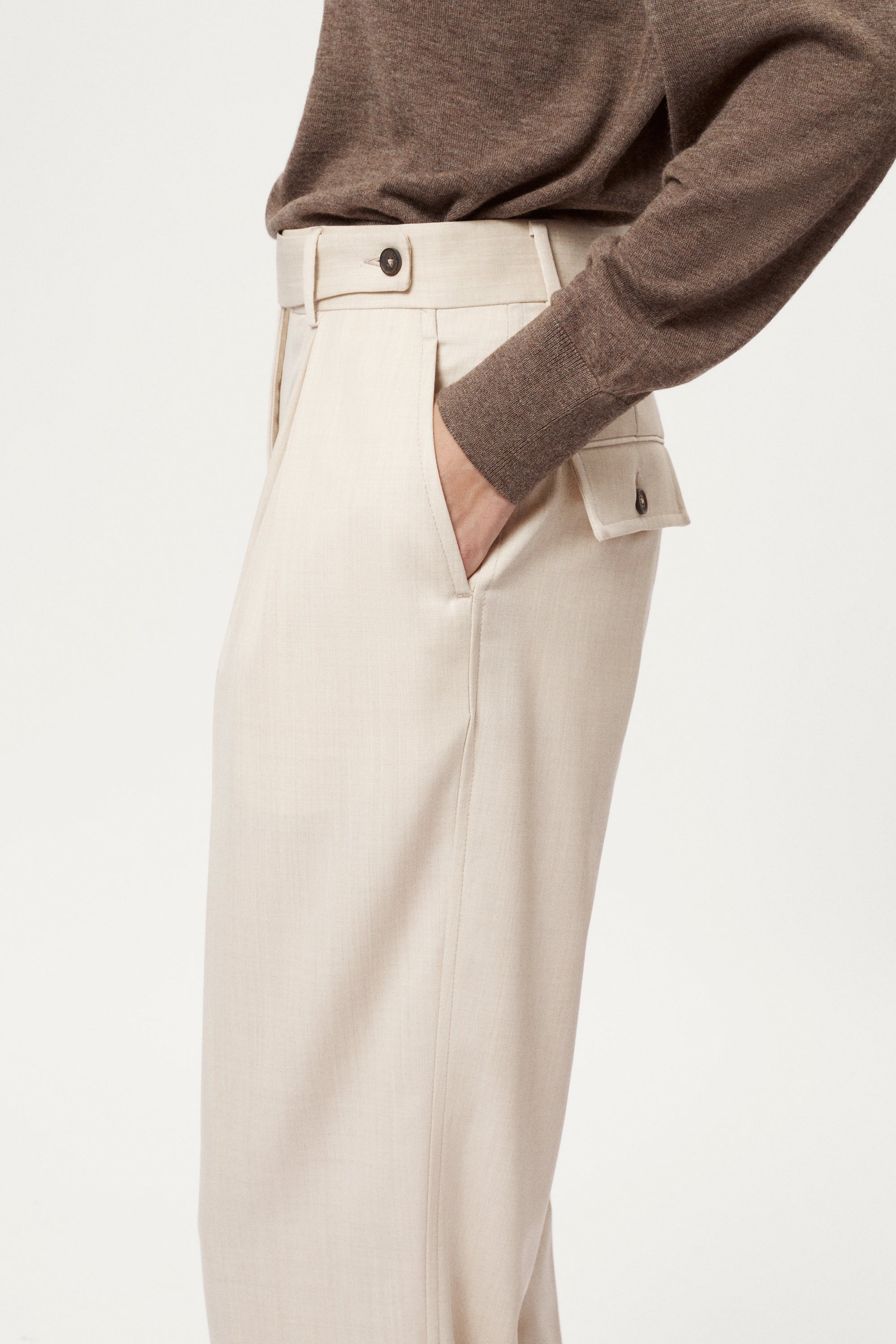 Beige pants worn with a brown sweater on a light background