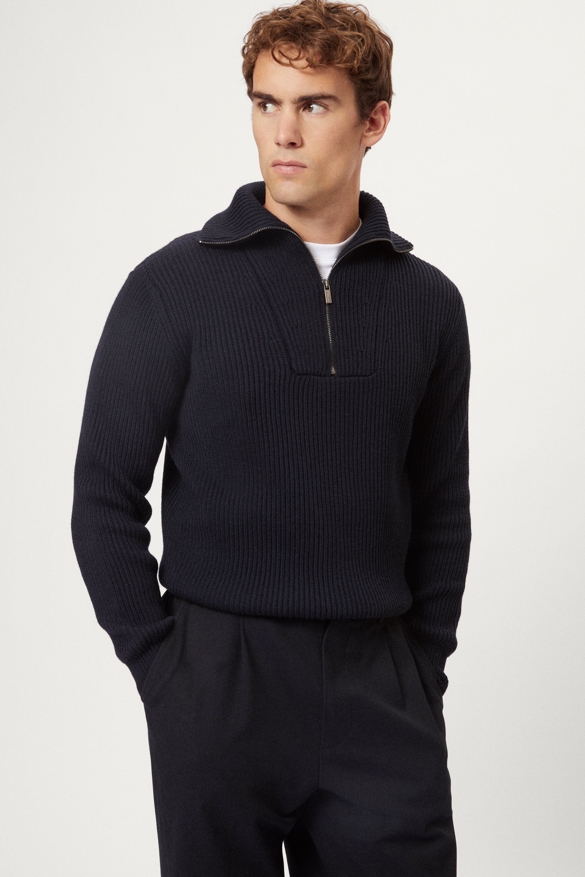 Man wearing a dark blue merino half zip sweater with a white background