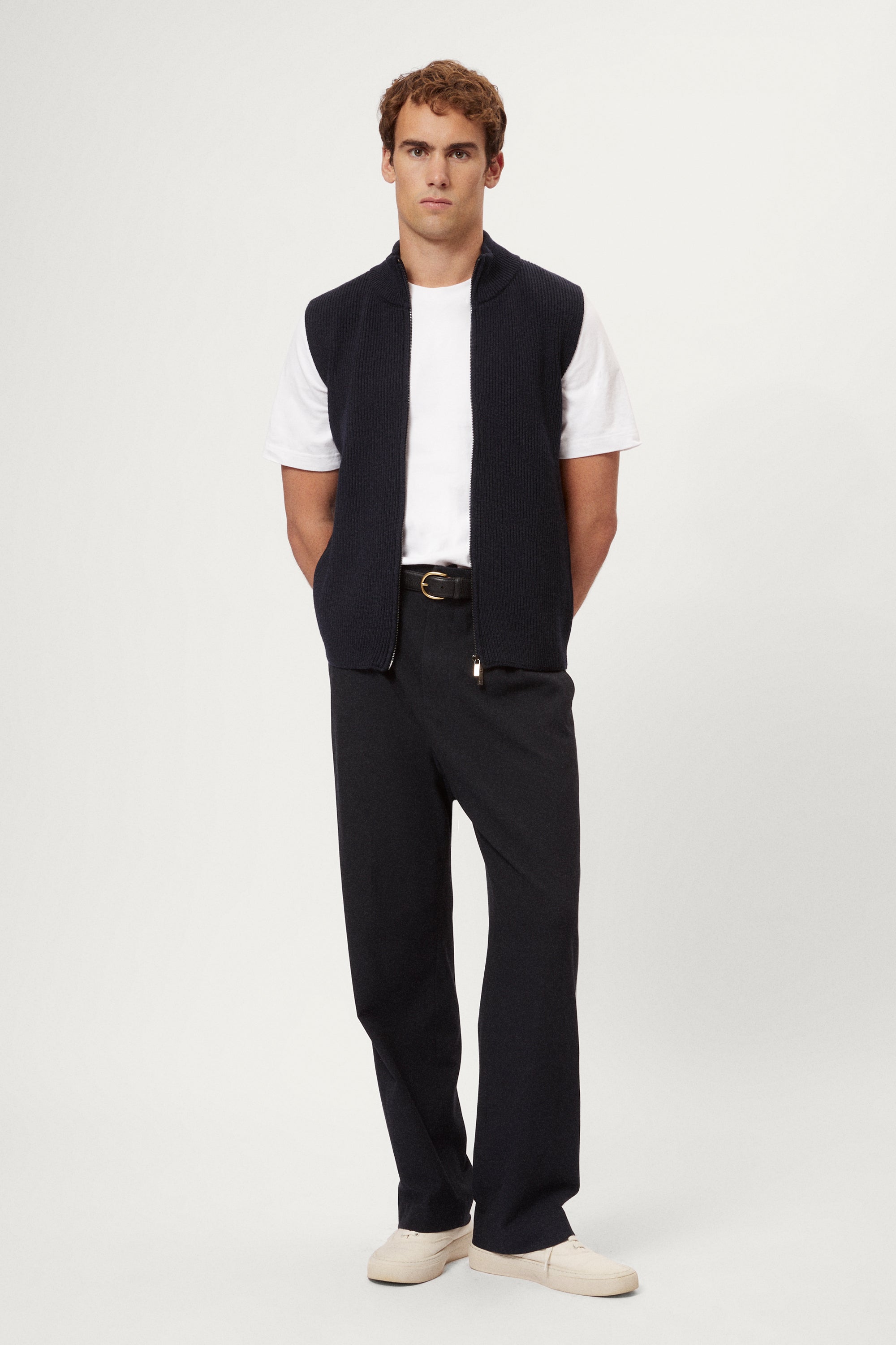 Man wearing a navy blue vest over a white shirt on a light gray background