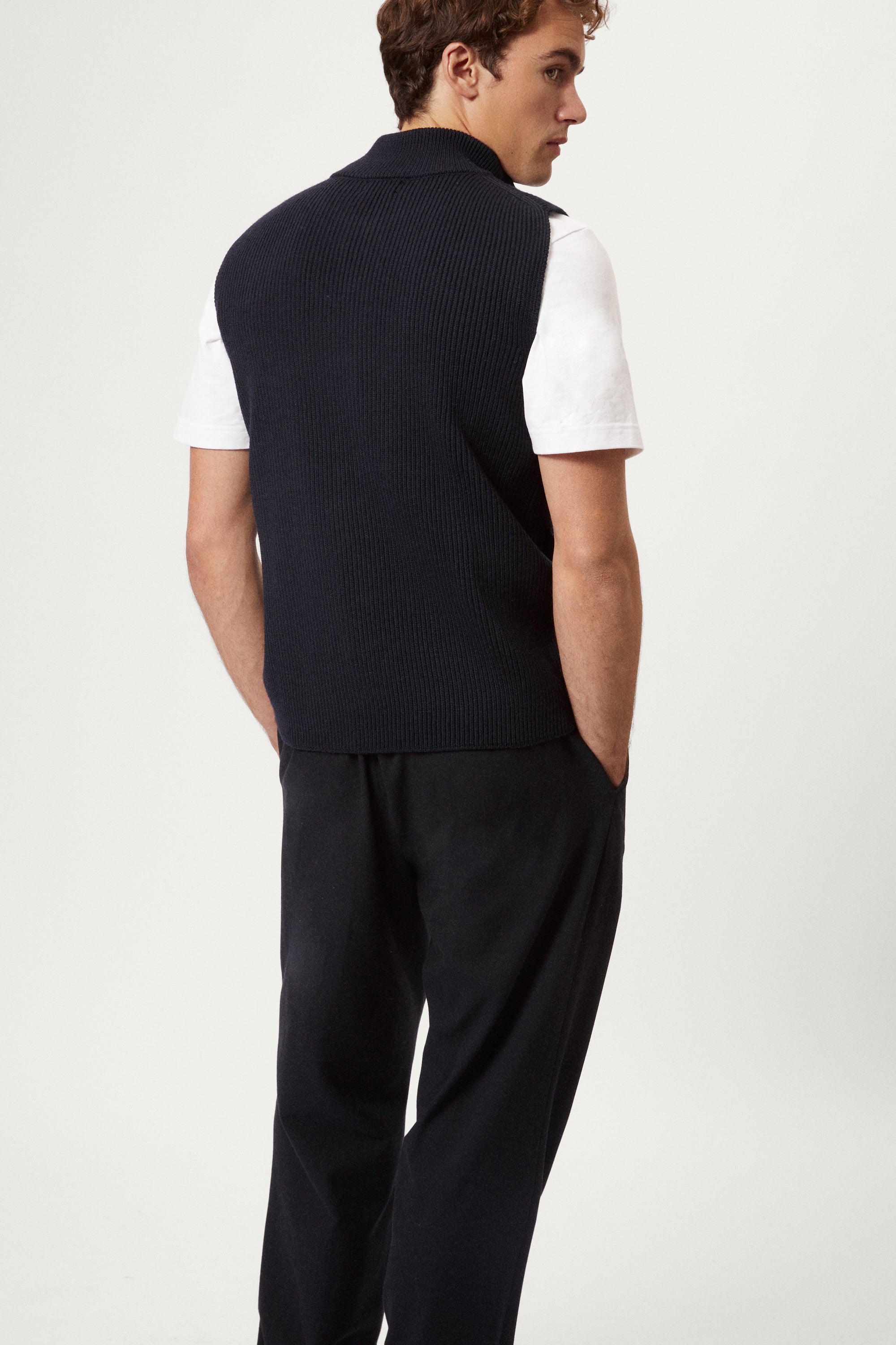 Man wearing a navy blue vest over a white shirt on a light gray background