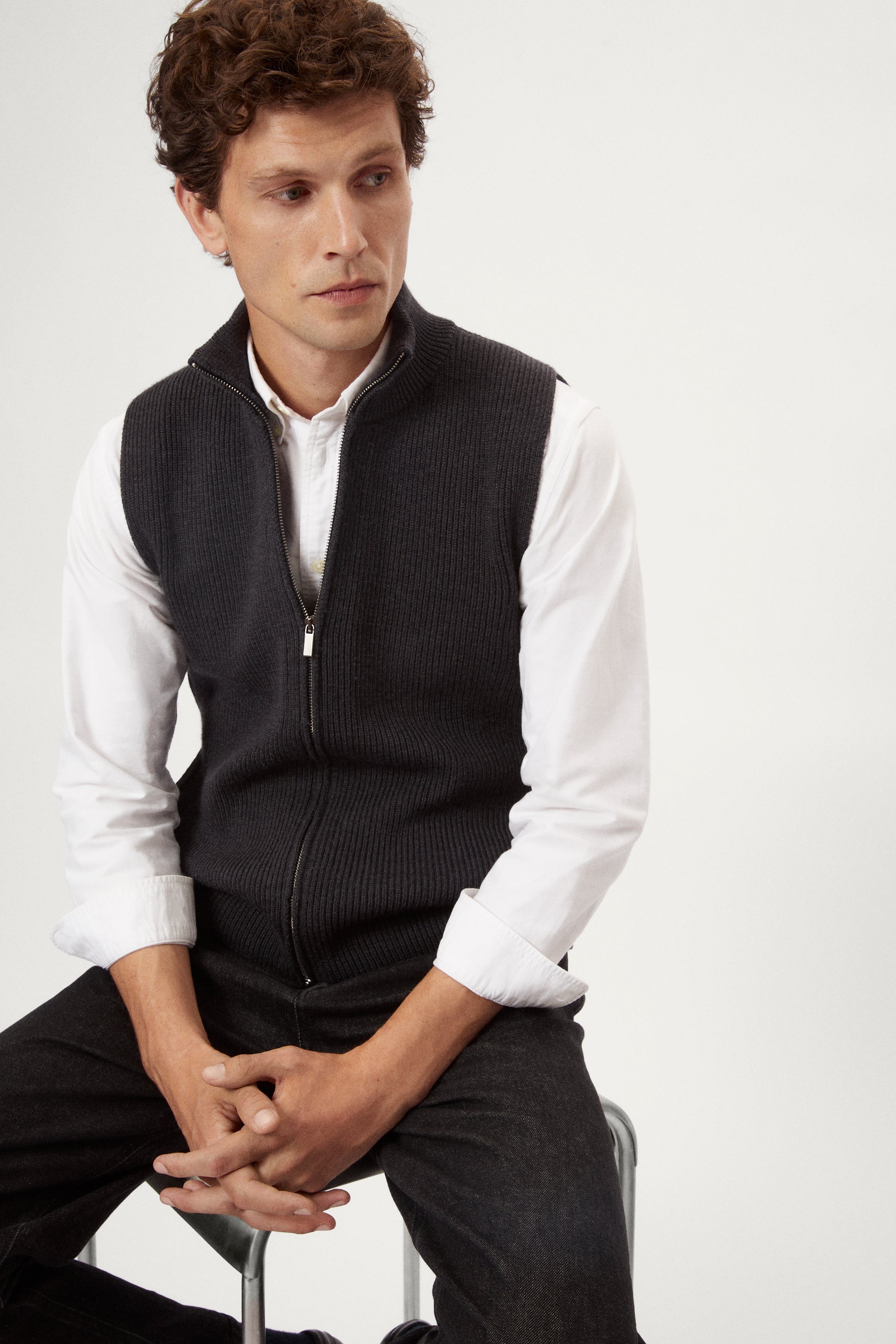 Man wearing a dark gray zip-up vest over a white shirt on a white background