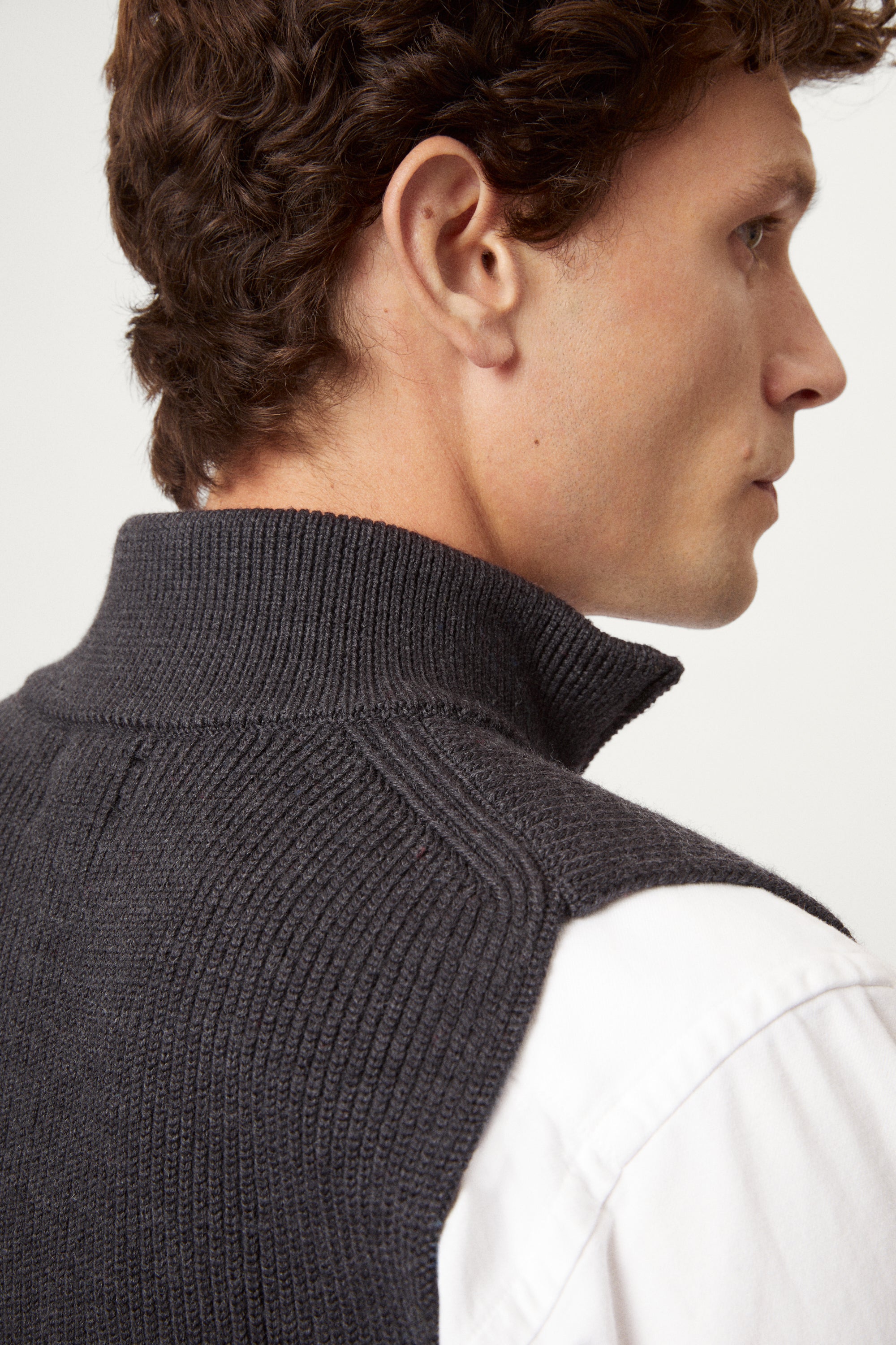 Man wearing a dark gray zip-up vest over a white shirt on a white background