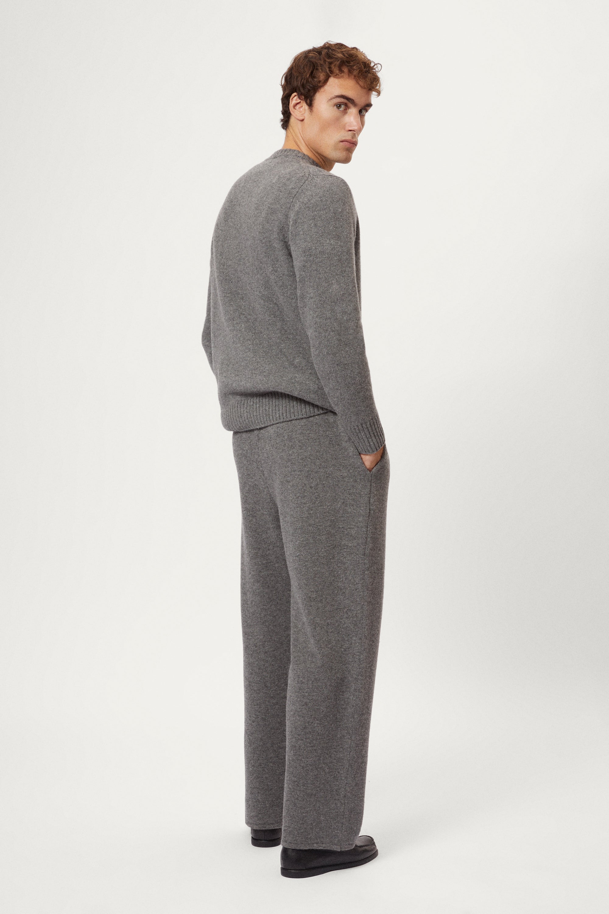 Person wearing a woolen gray knit pants and black shoes on a white background
