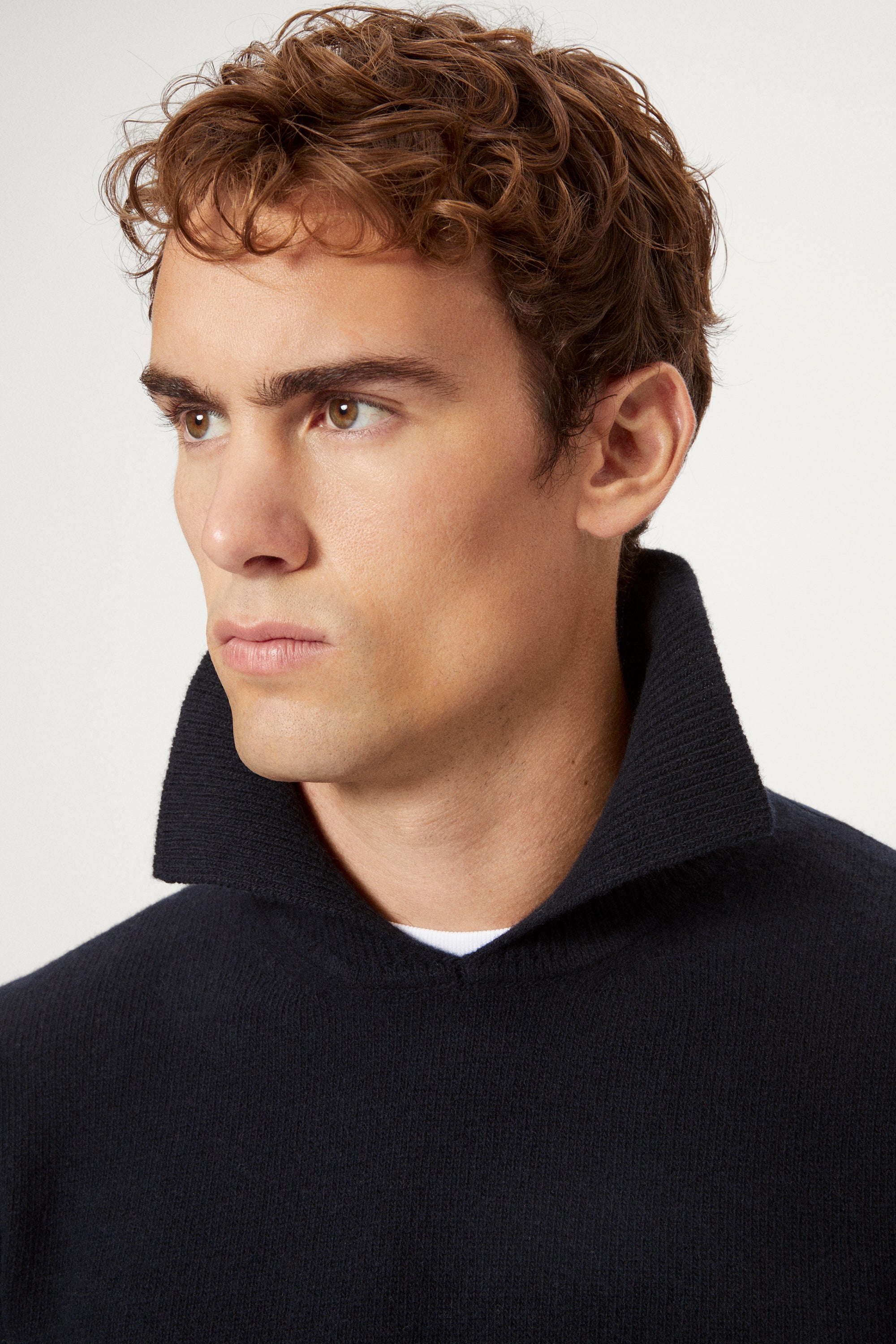 Man wearing a blue navy woolen polo sweater with a white background