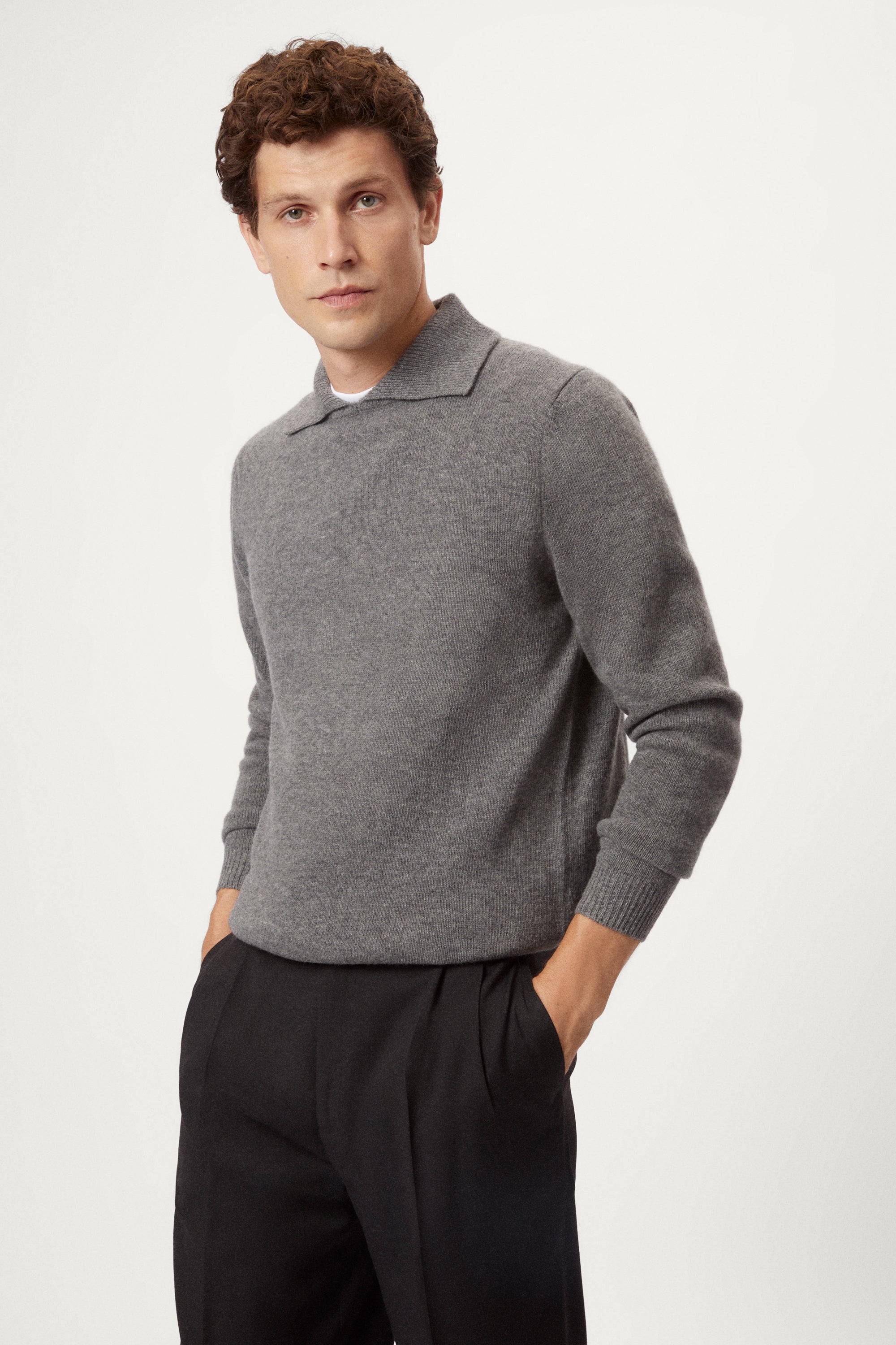 Man wearing a gray woolen polo sweater and black pants on a white background