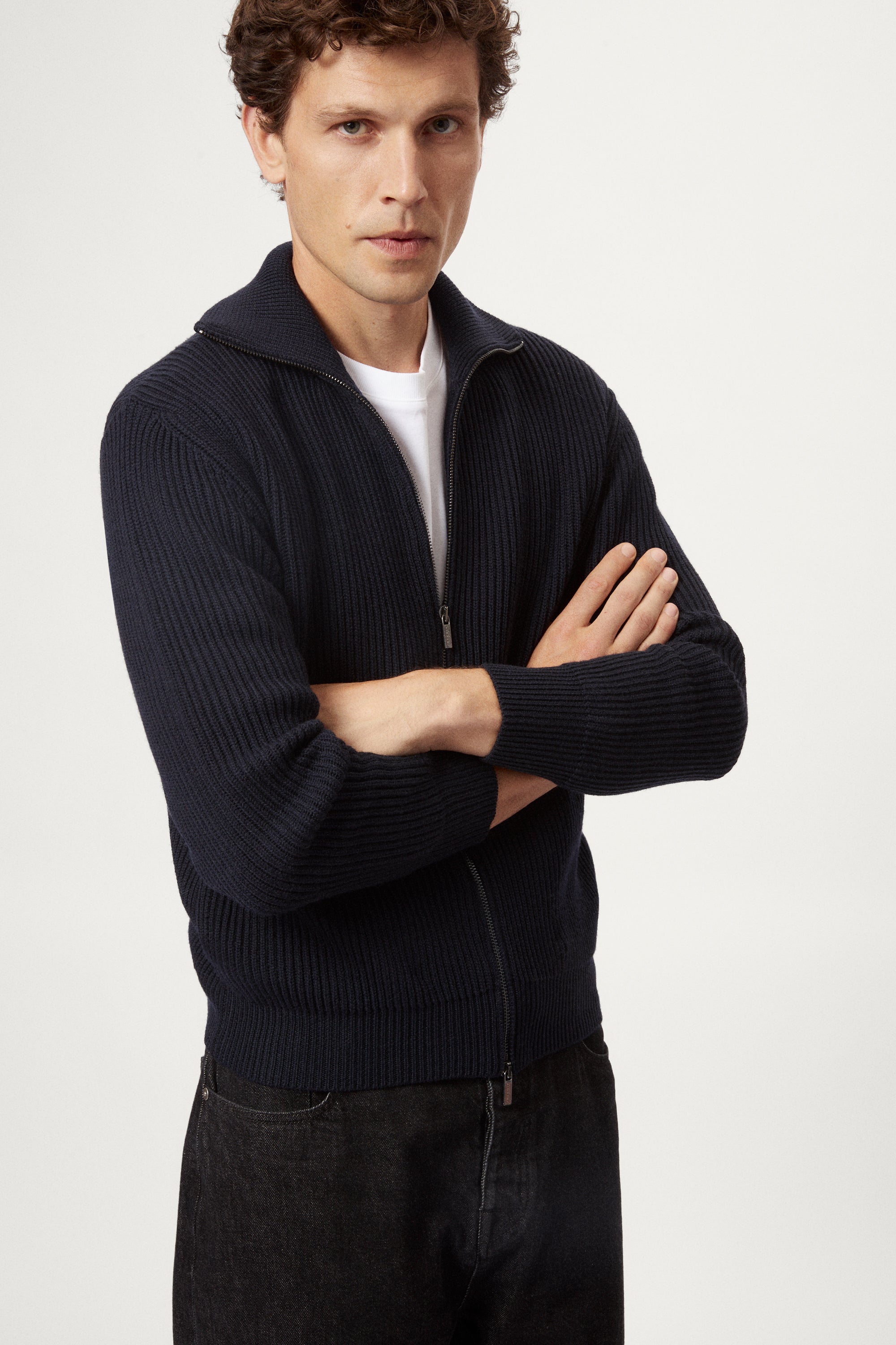 Man wearing a dark blue zip-up sweater over a white shirt on a light gray background