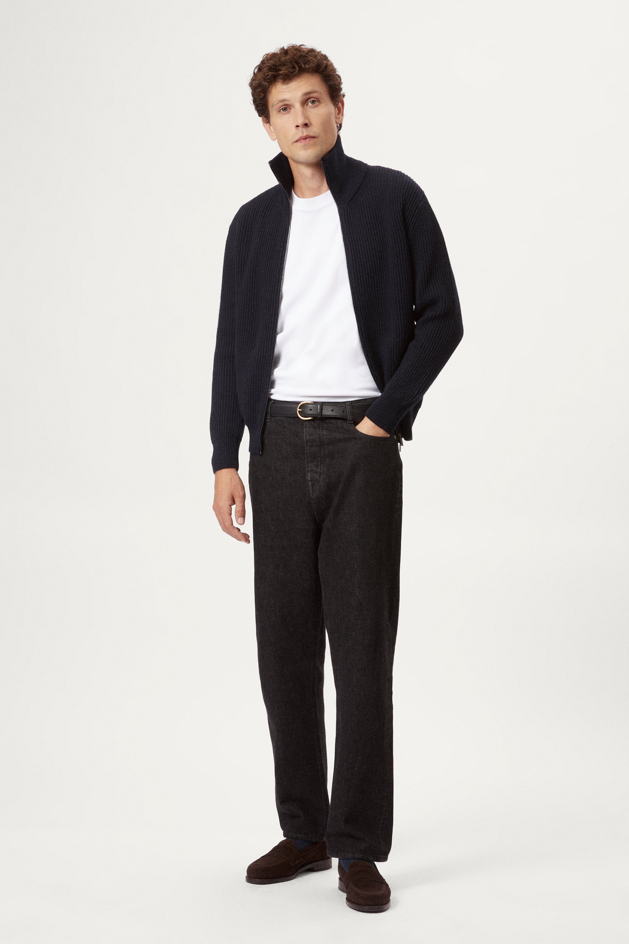 Man wearing a dark blue zip-up sweater over a white shirt on a light gray background