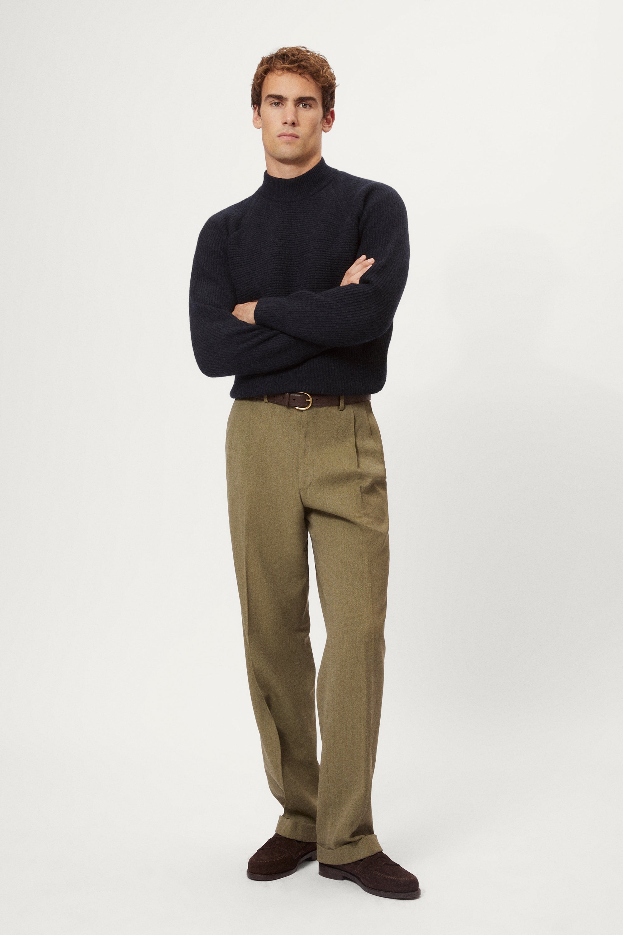 Man wearing a dark blue woolen ribbed sweater and green pants on a white background