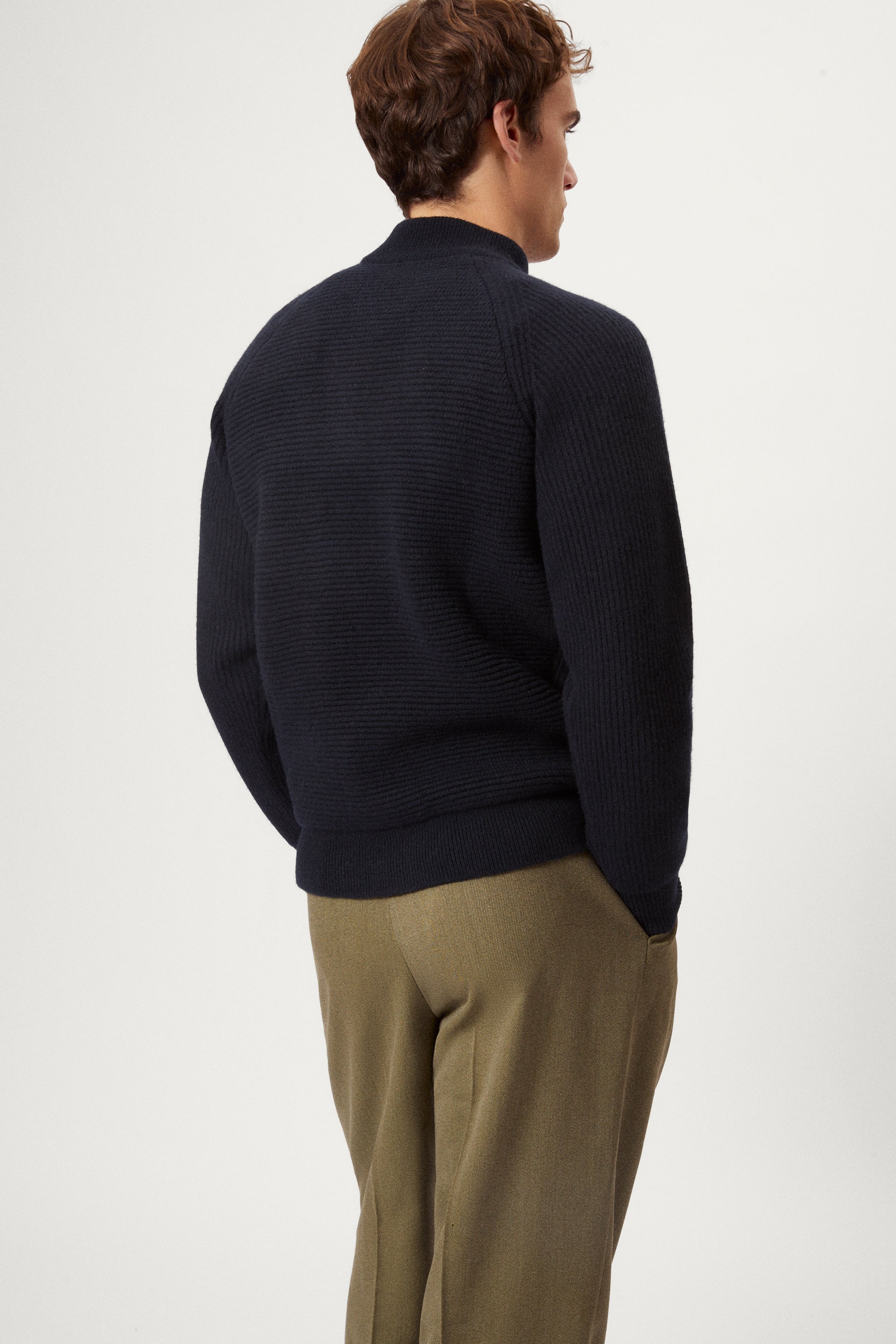 Man wearing a dark blue woolen ribbed sweater and green pants on a white background