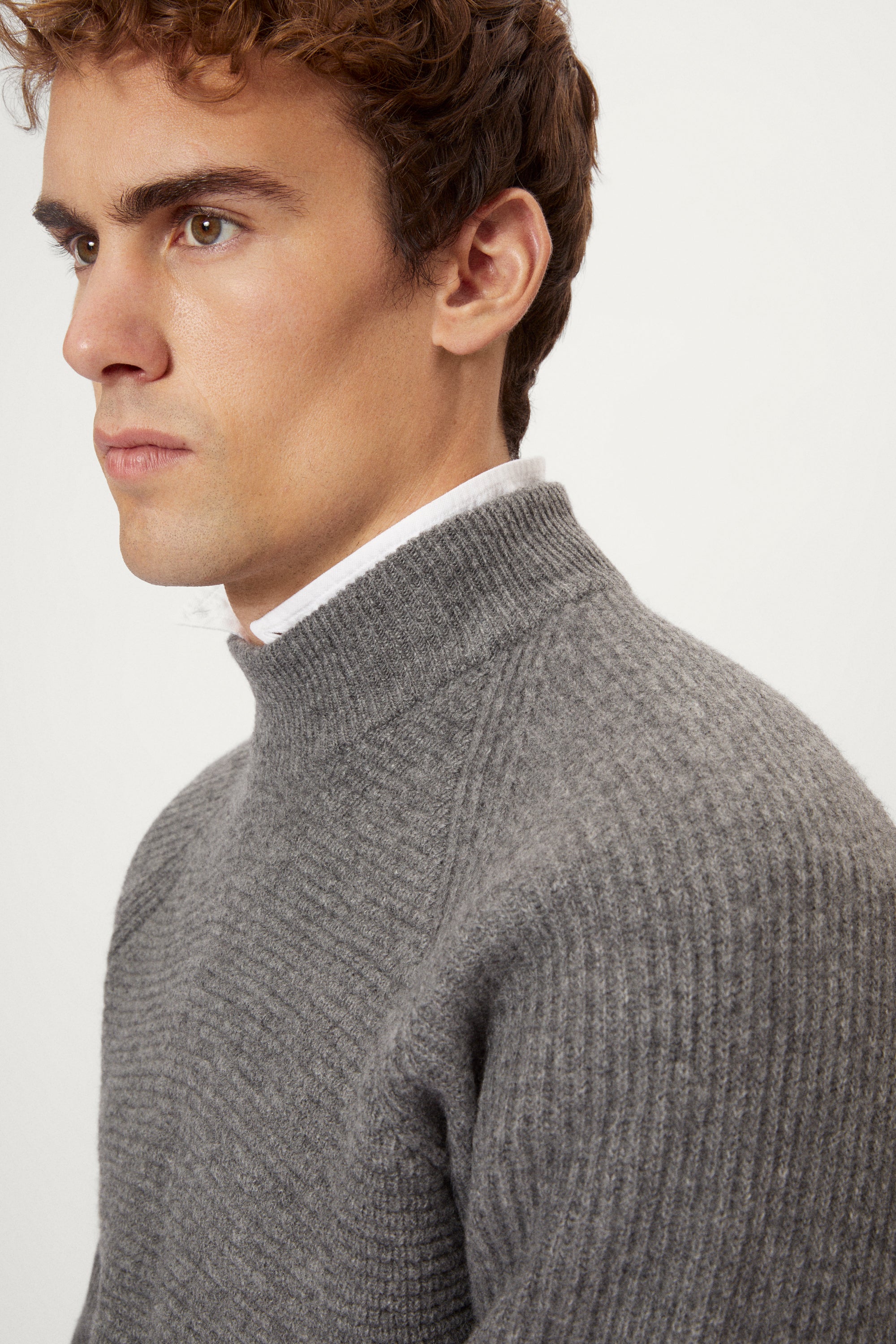 Man wearing a gray ribbed sweater and white pants on a light background