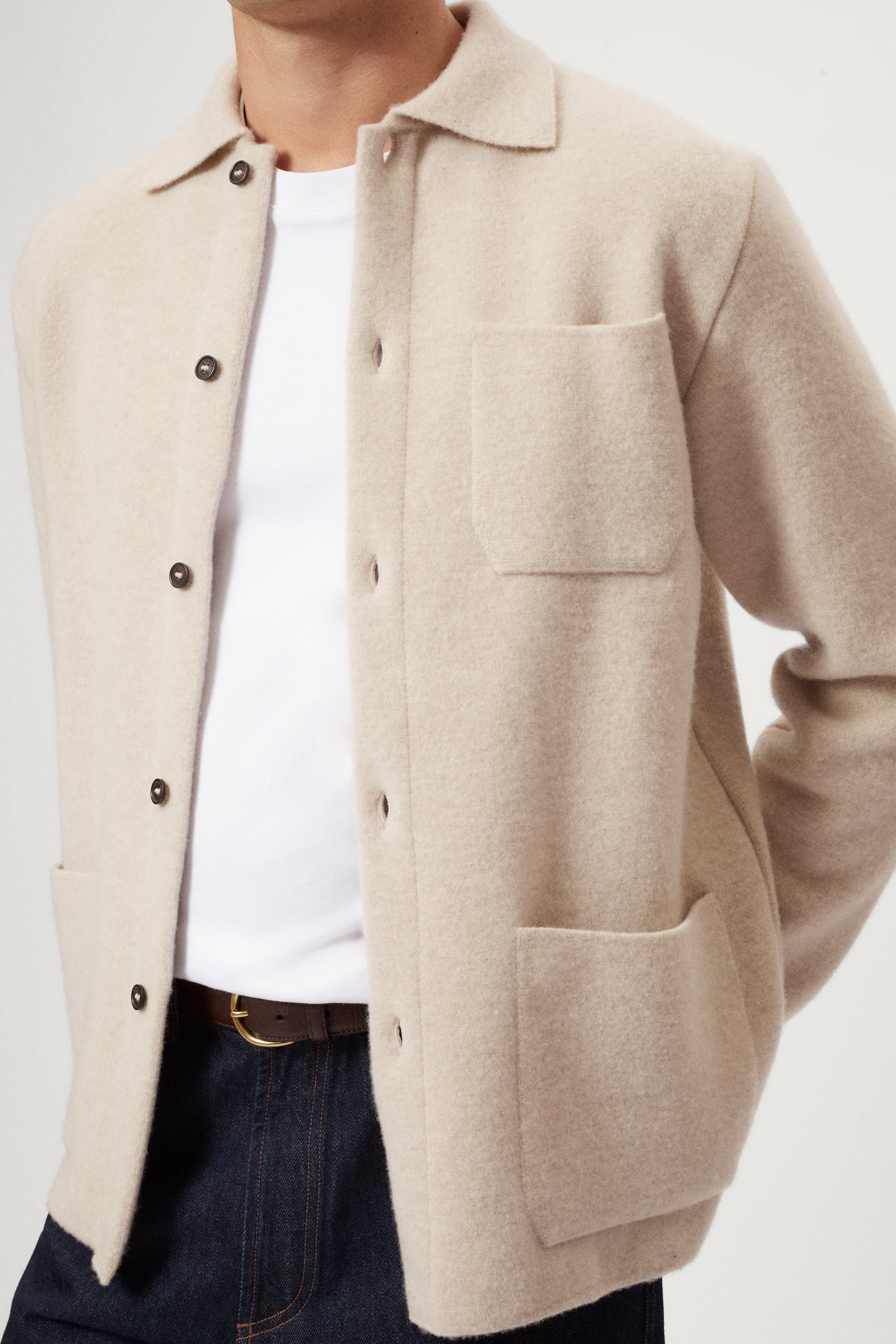 Person wearing a beige Boiled Wool Jacket over a knit sweater with a plain background