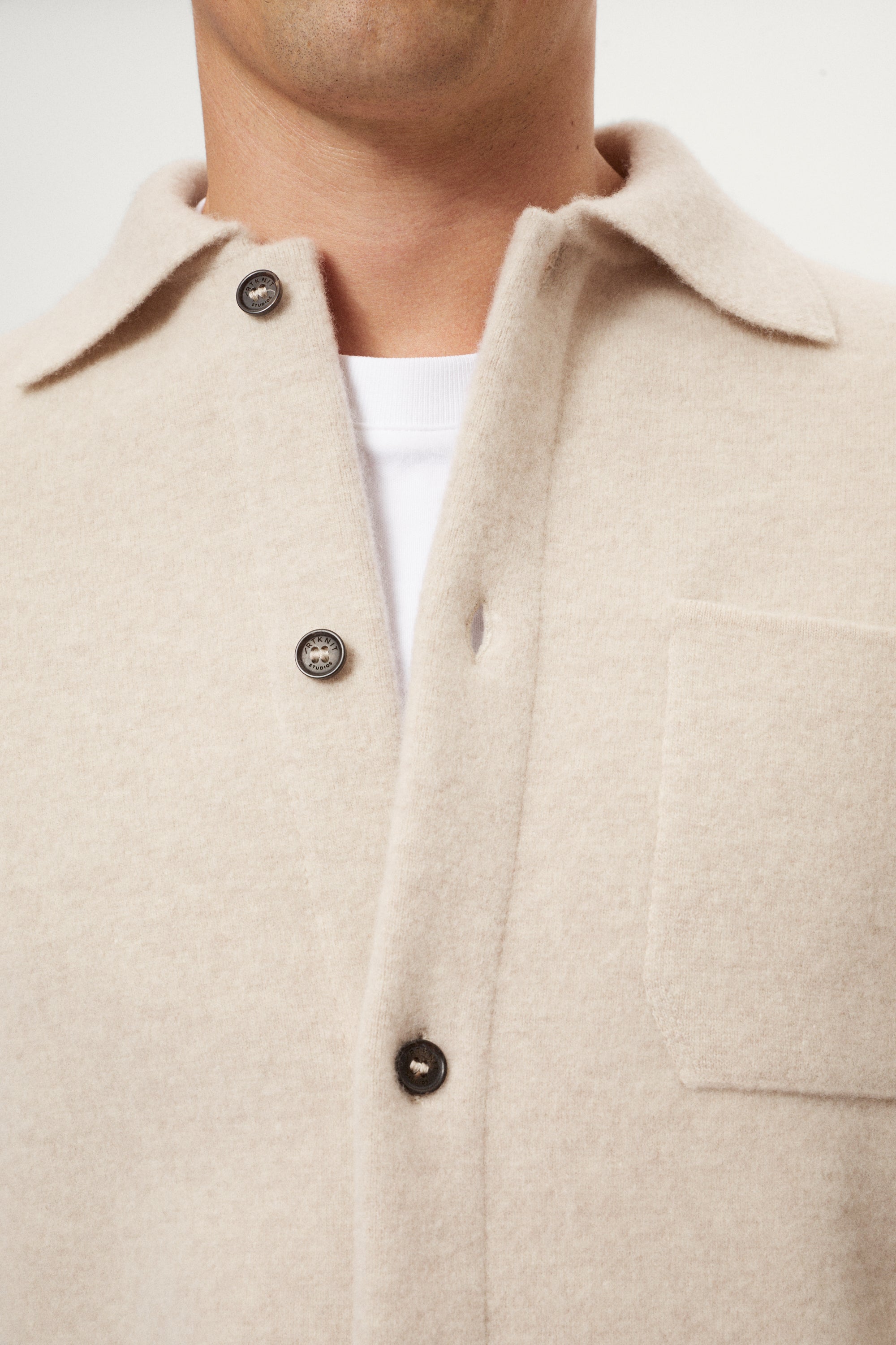 Close-up of a beige boiled wool jacket with button details on a neutral background