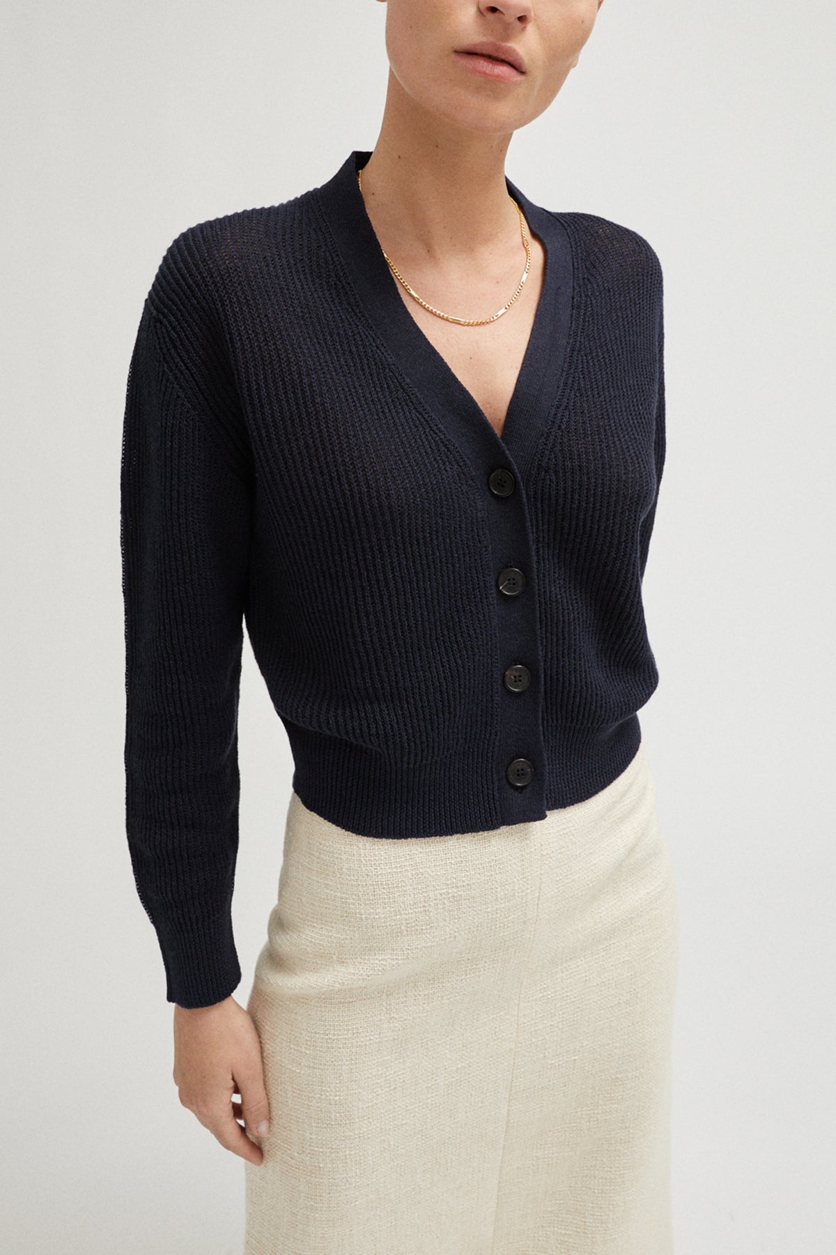 Person wearing a navy blue cardigan over a beige skirt on a light gray background