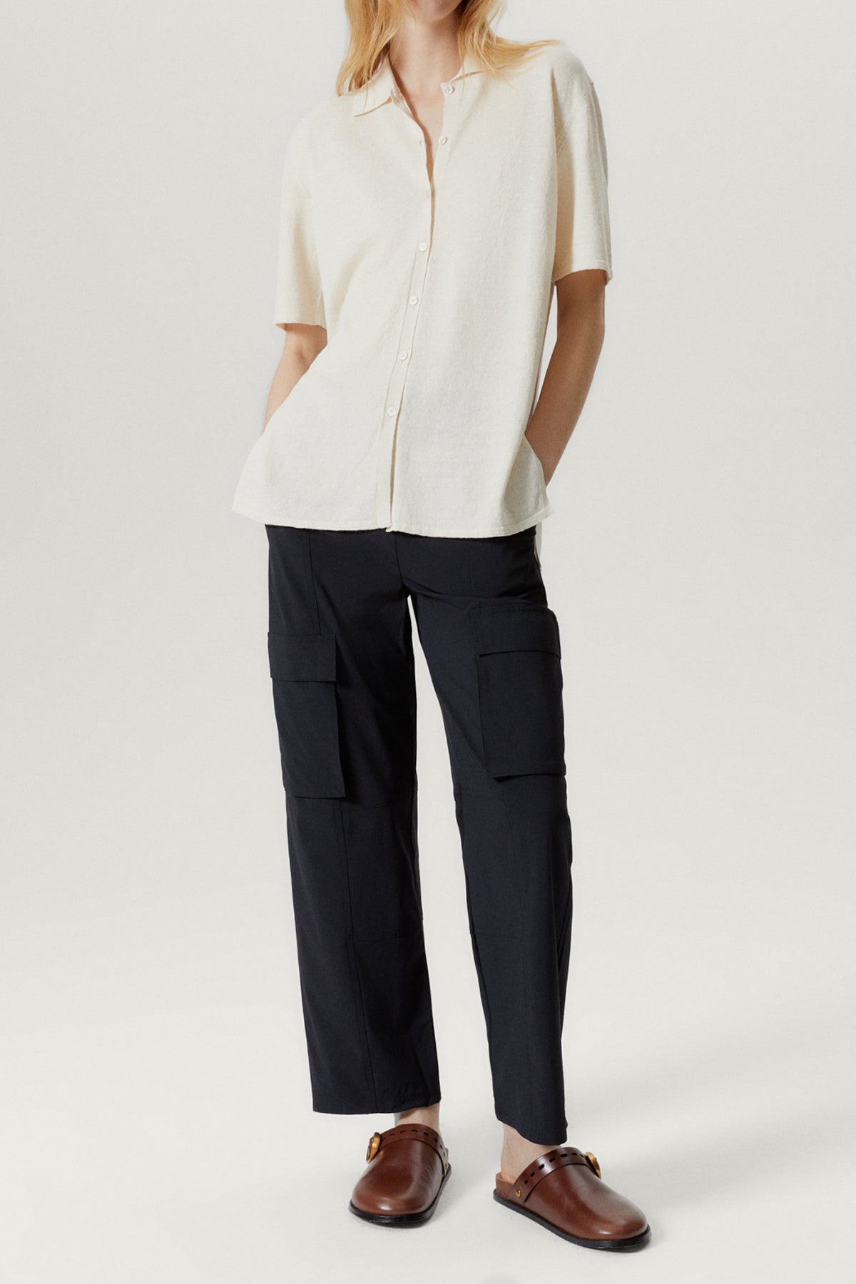 Person wearing a white shirt and dark cargo pants on a white background