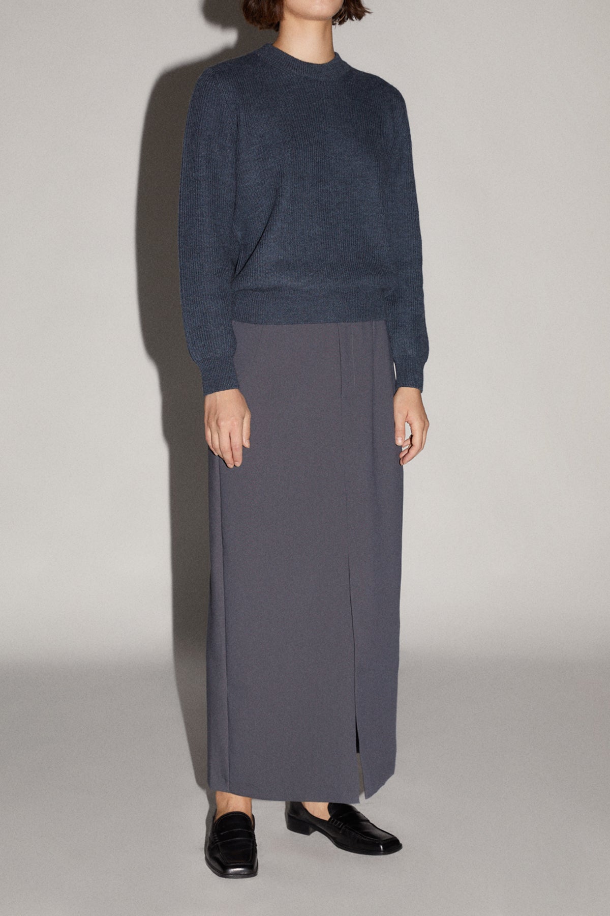 Person wearing a dark blue sweater and gray skirt on a plain background