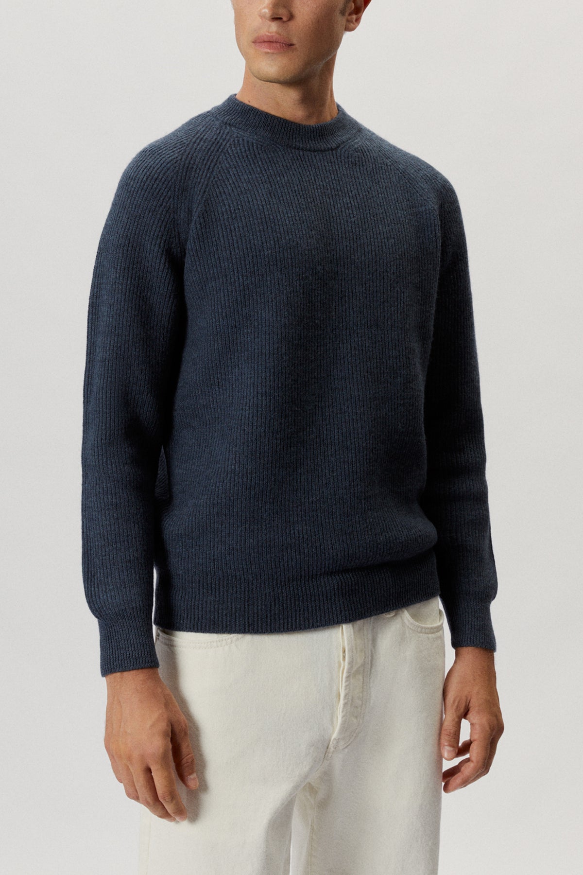 Man wearing a dark blue sweater and white pants on a light gray background