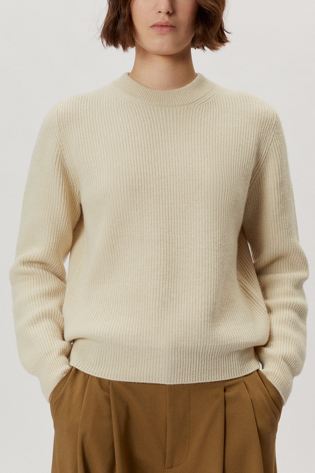 Person wearing a natural dye sweater juniper ecru sweater and brown pants on a white background