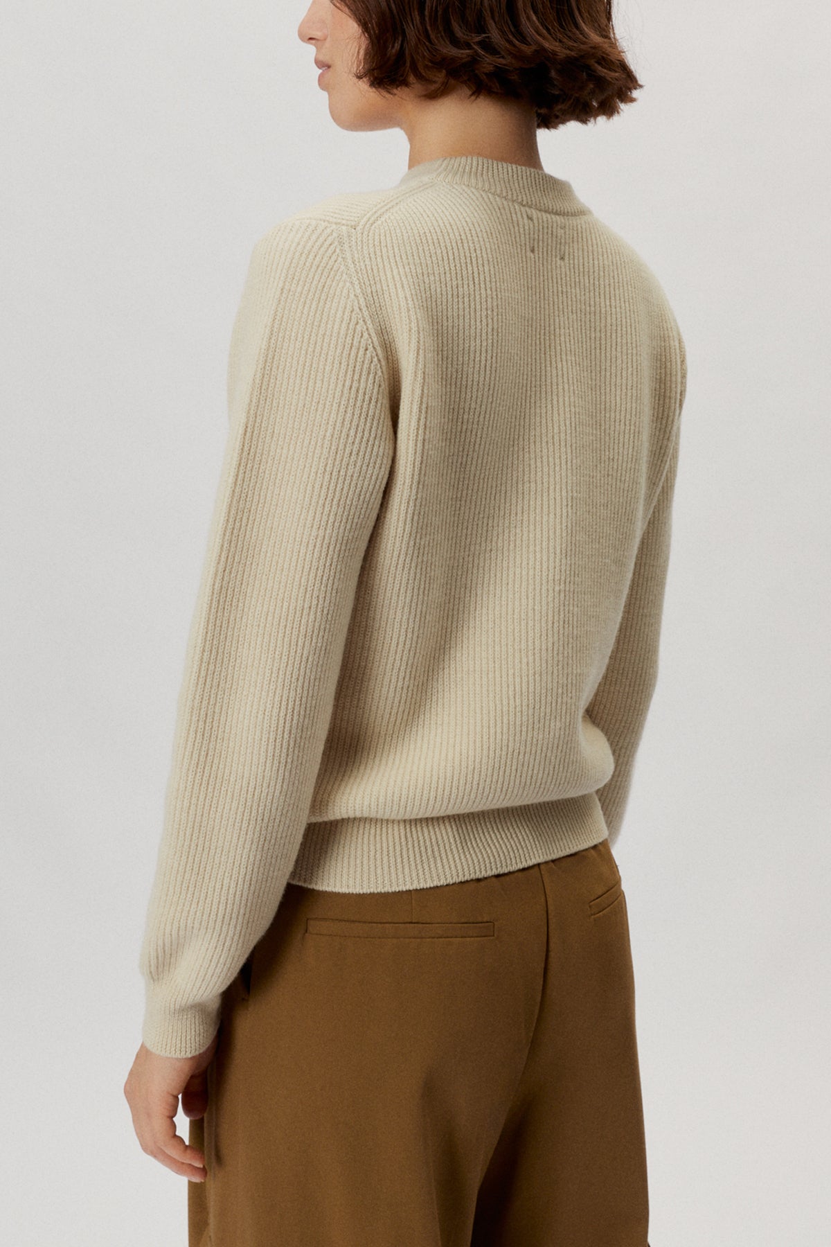 Person wearing a beige sweater and brown pants on a white background