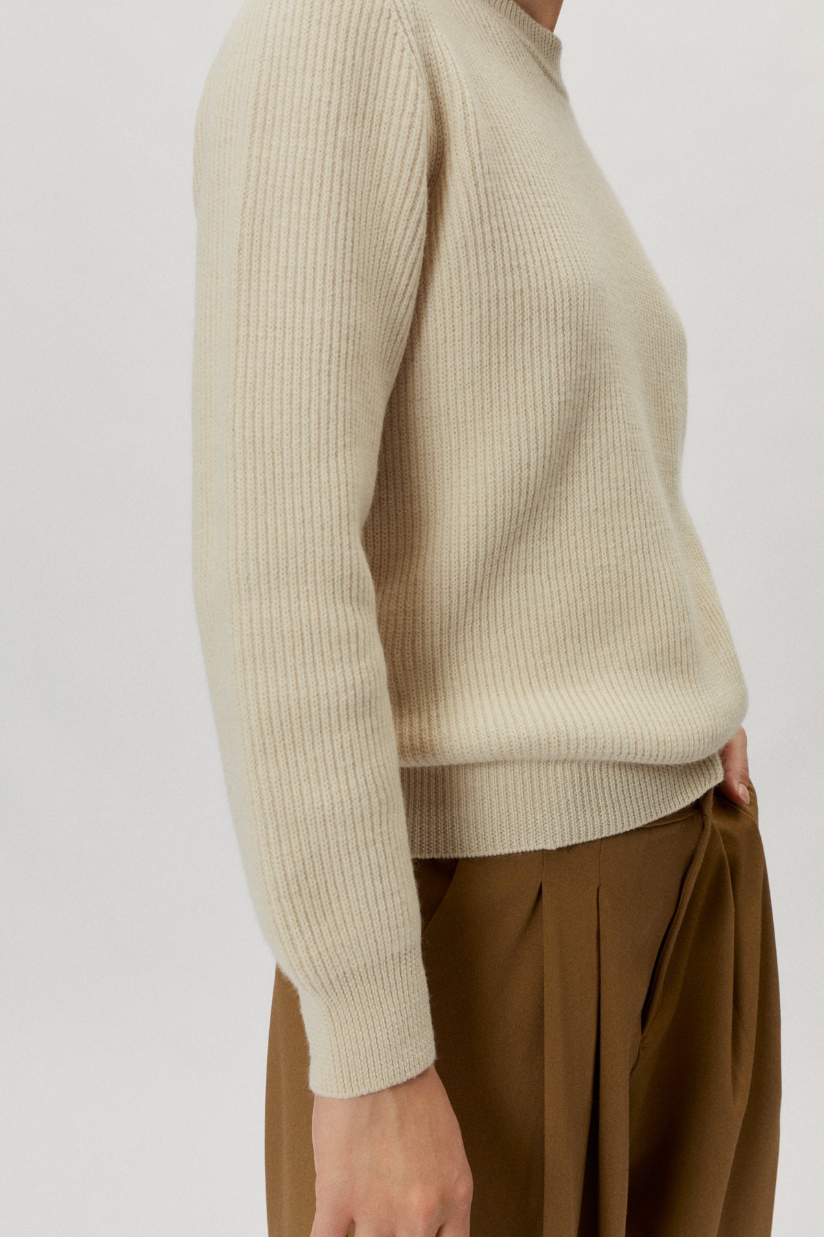 Person wearing a beige ribbed sweater and brown pants on a white background