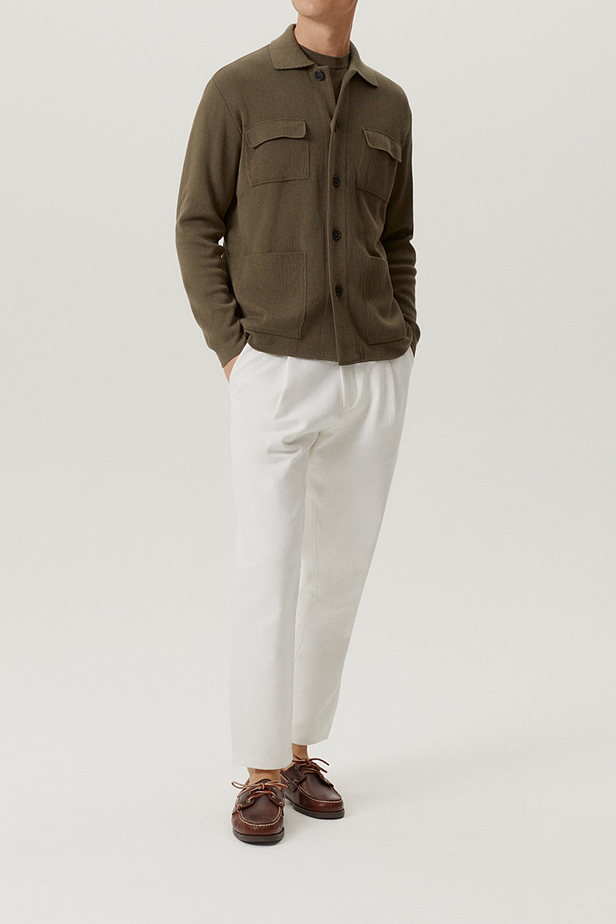 Person wearing a green jacket and white pants on a light gray background