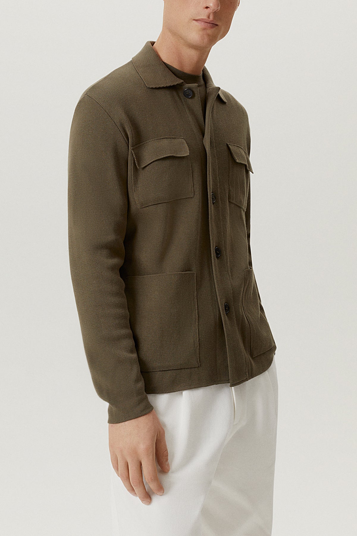 Man wearing a green jacket and white pants on a light gray background