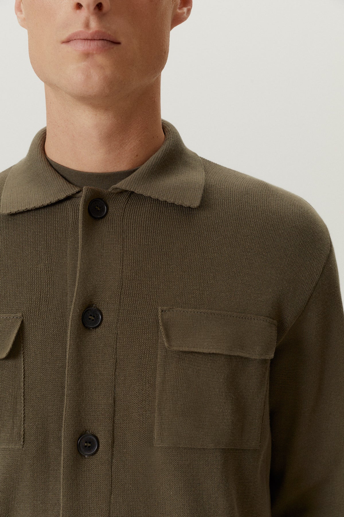 Close-up of a person wearing a brown jacket with button details on a plain background