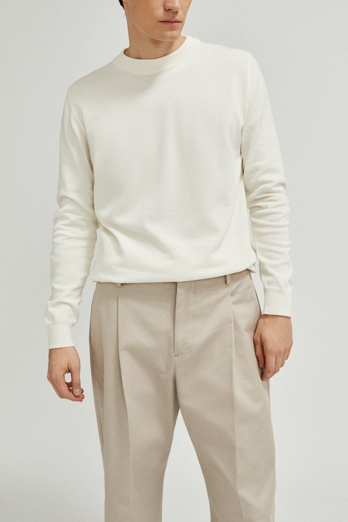Person wearing a white sweater and beige pants on a plain background