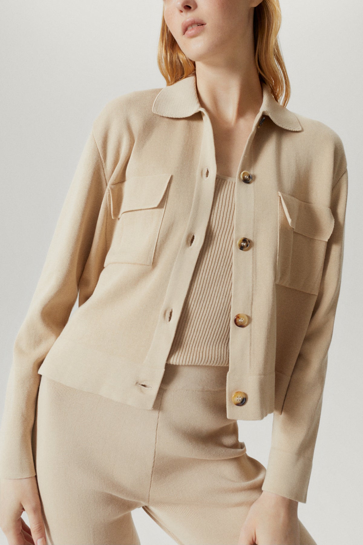 Person wearing a beige jacket and pants on a plain background