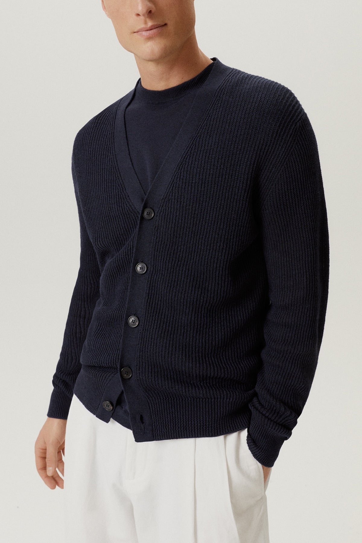 Man wearing a linen blue cardigan shirt with white pants on a light gray background